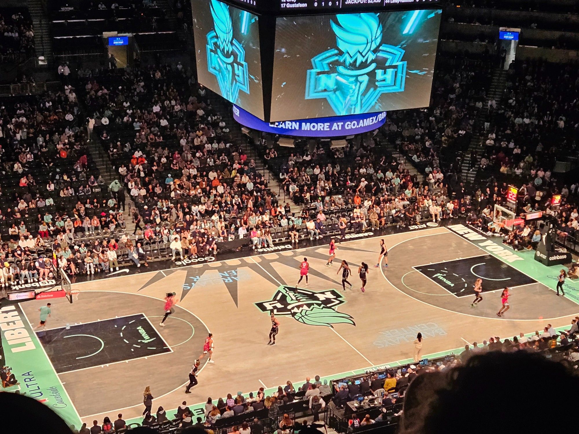 An image of a basketball game being played between the New York Liberty and the Las Vegas Aces. This picture is taken from a high angle and in line with the baseline.