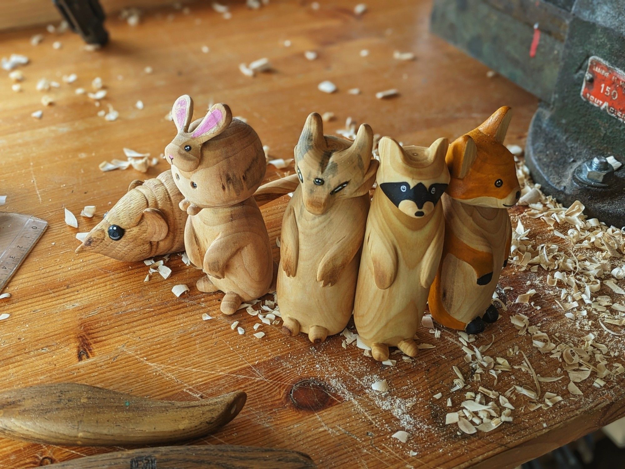 Group of woodcarved critters, a elephant eared shrew, monster with a whole plump rabbit as its head, a gargoyle with three eyes, a racoon and a fox