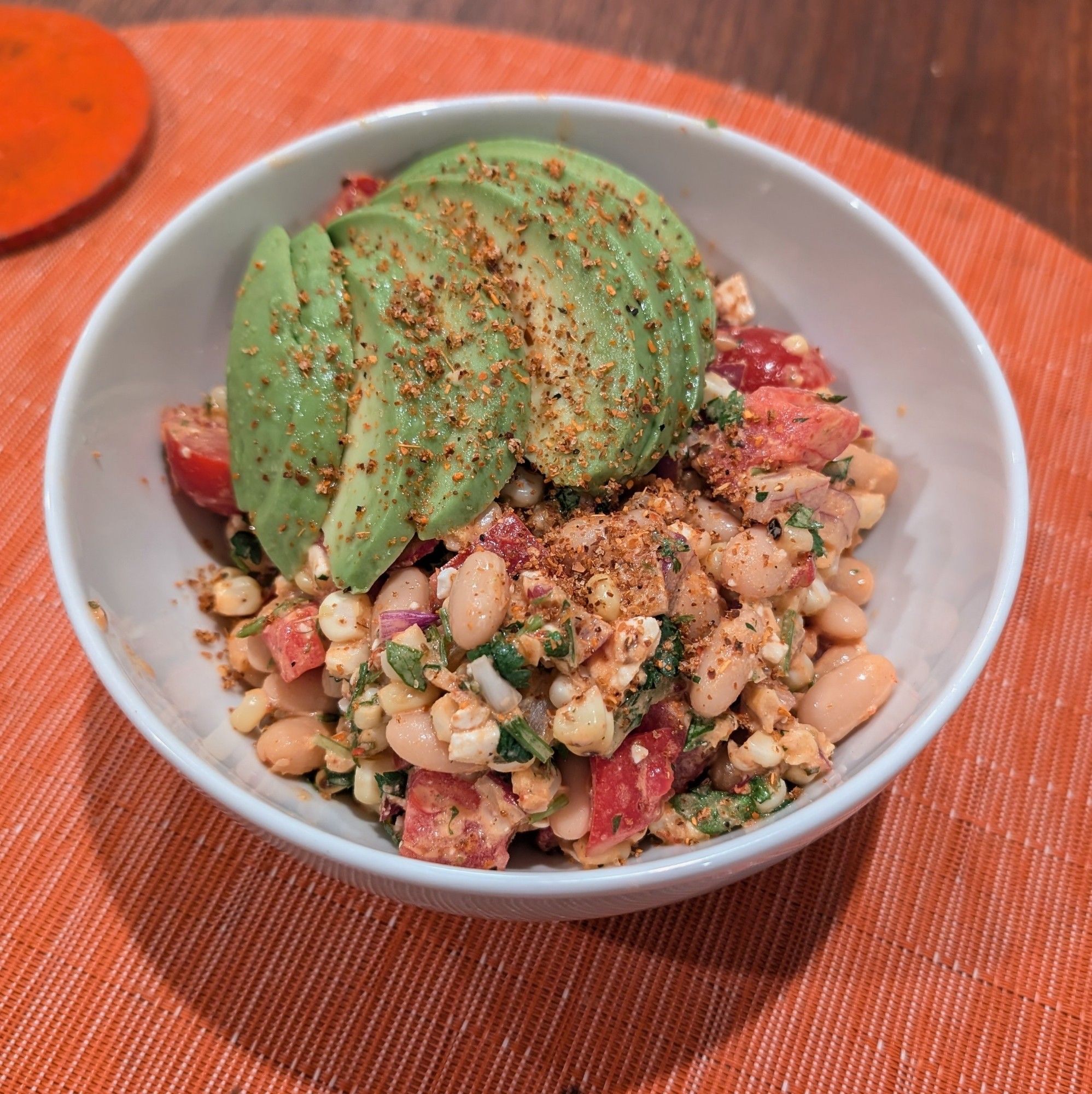 A bowl full of bean salad in a creamy dressing containing charred corn, tomatoes, sliced radishes, red and green bell pepper, red onion, and cilantro topped with fanned out on top