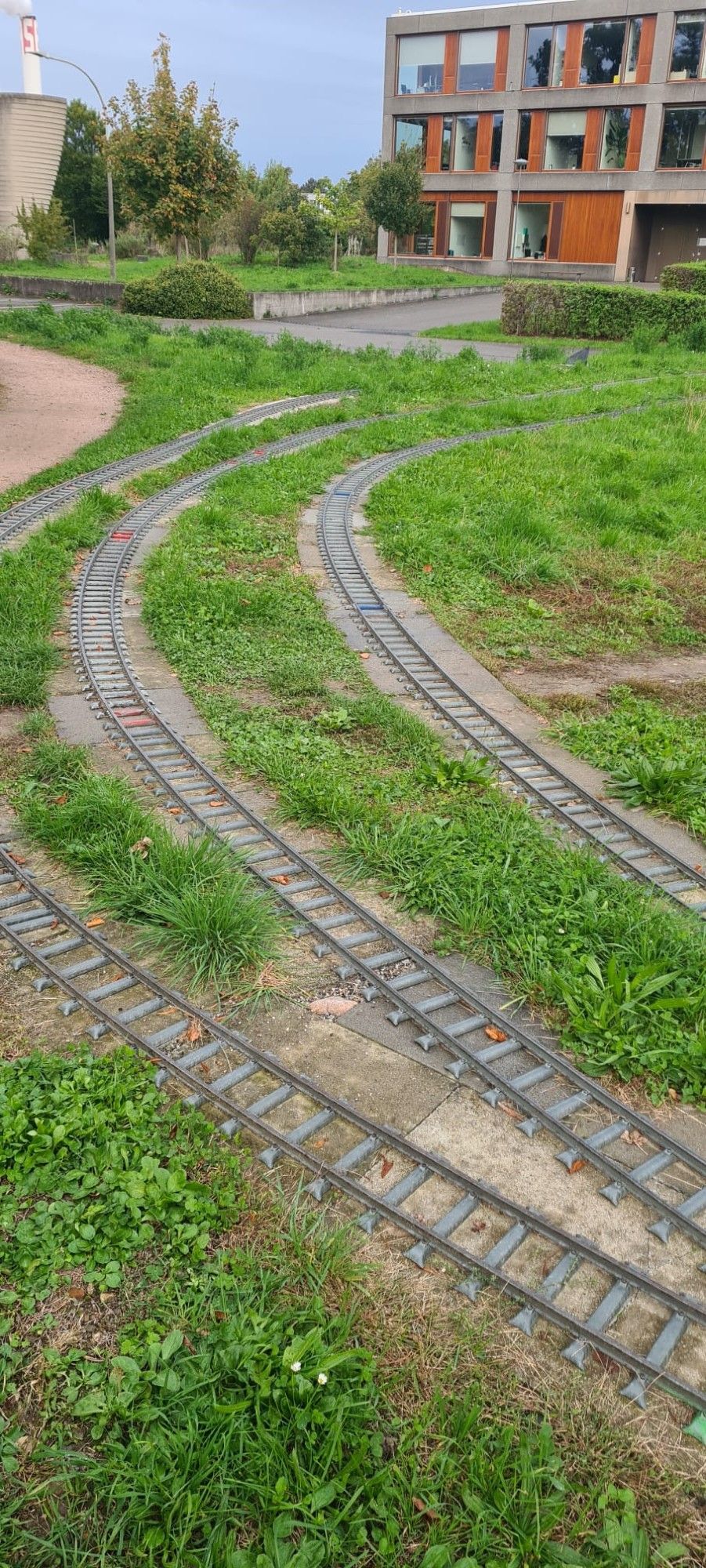 jeu de rails miniatures  passant devant un immeuble d'habitation, entourés de gazon.