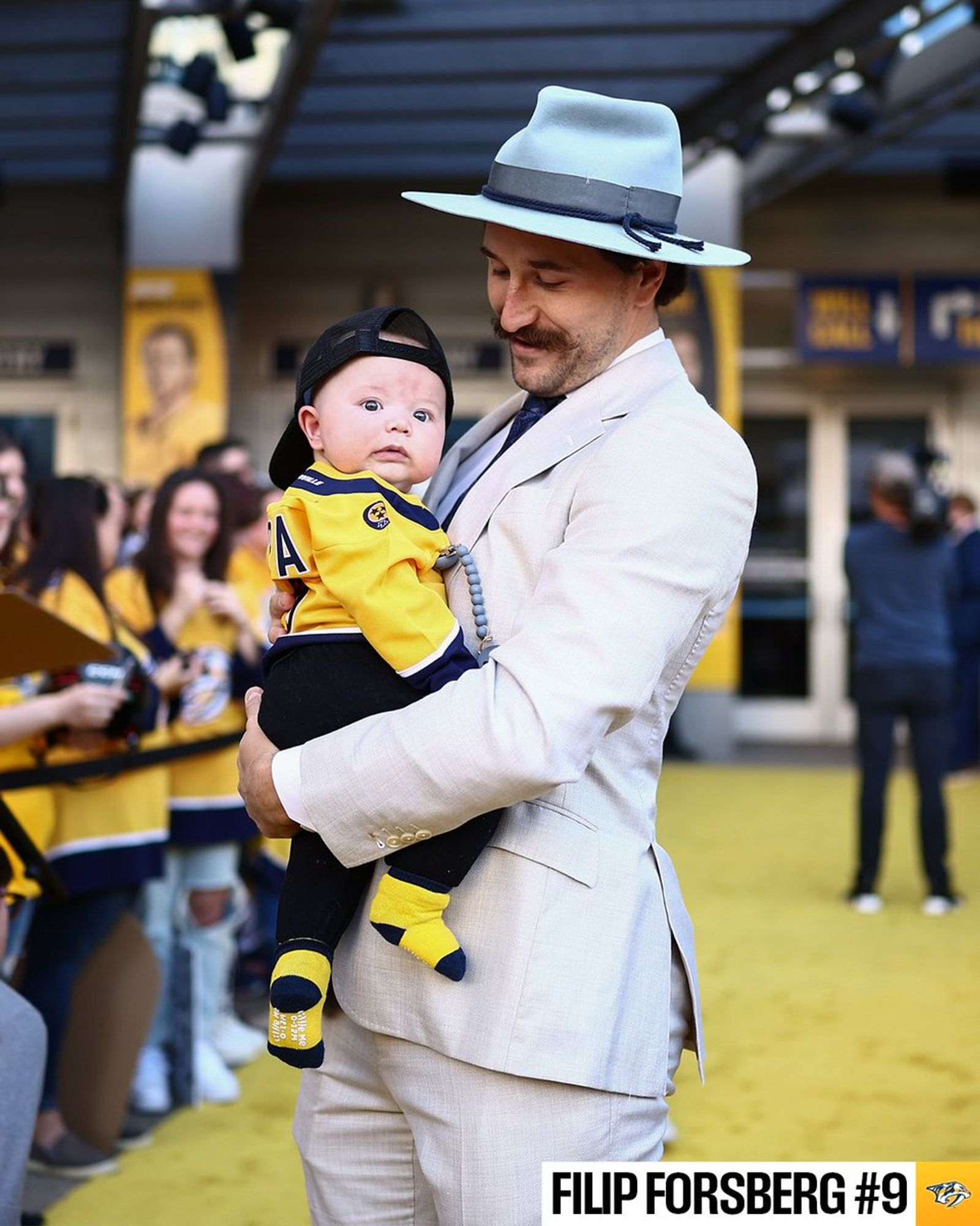 Filip Forsberg walking the yellow carpet ahead of the Predators home opener holding his child.