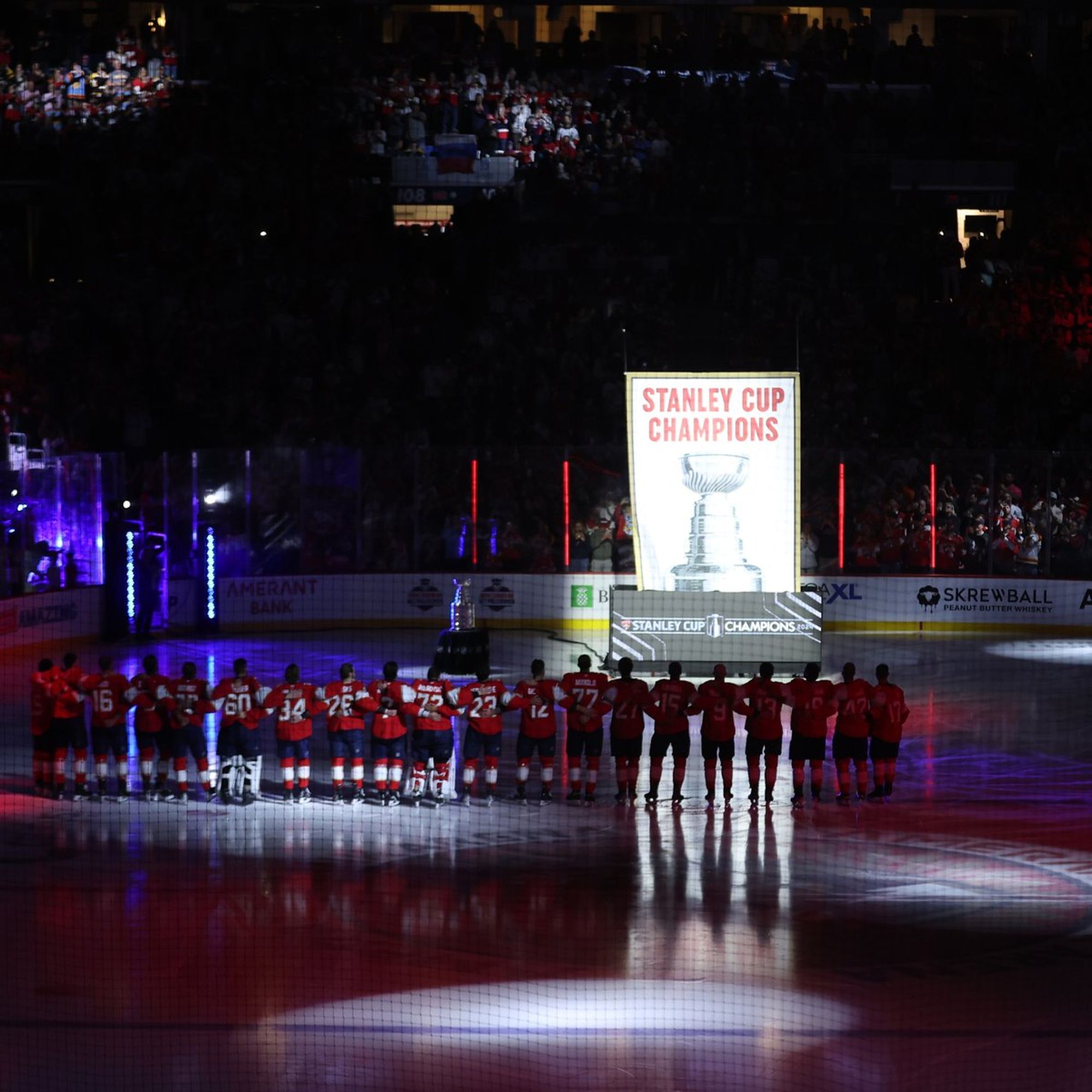 Photo of Florida Panthers players looking on as their Stanley Cup championship banner is raised.