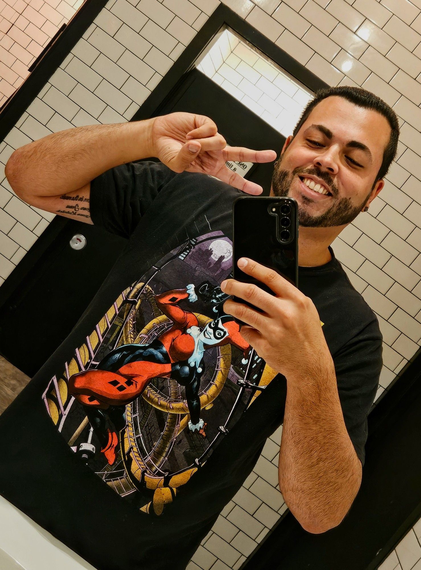 A bathroom selfie of a smiling Puerto Rican male wearing a Harley Quinn t-shirt as he prepares to see Joker: Folie a Deux