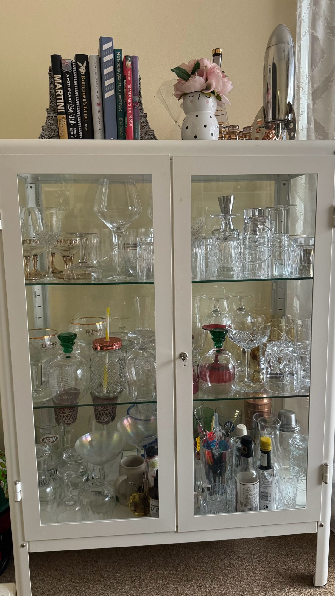 An IKEA glass-walled white cabinet, full of glassware of various sizes and styles.