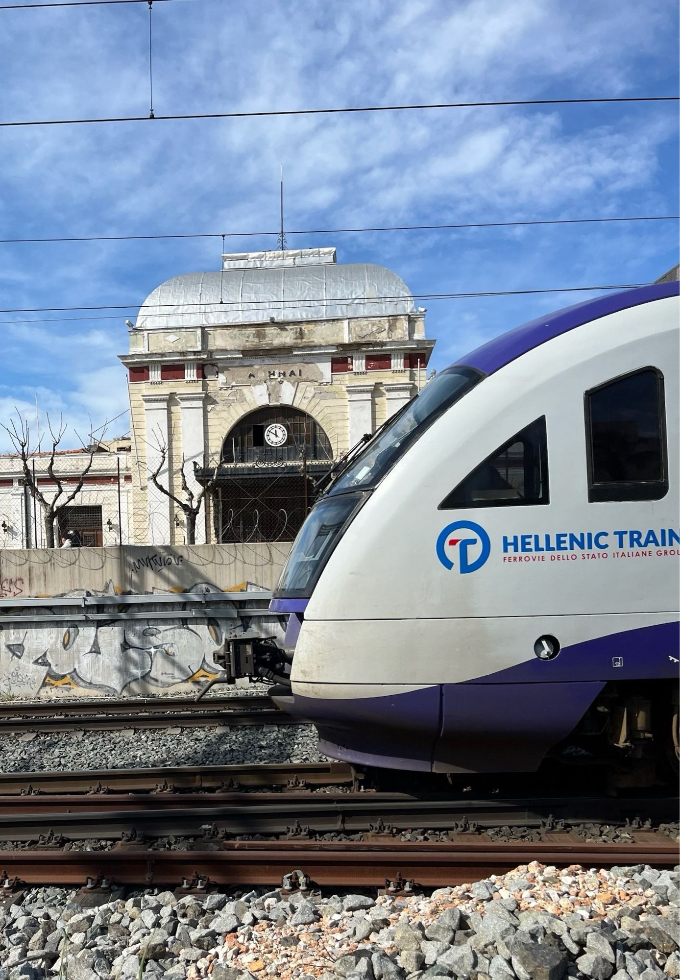 An abandoned late 19th Century train station in the belle époque style, clock stopped, plasterwork decaying, with a modern train passing in front from the right