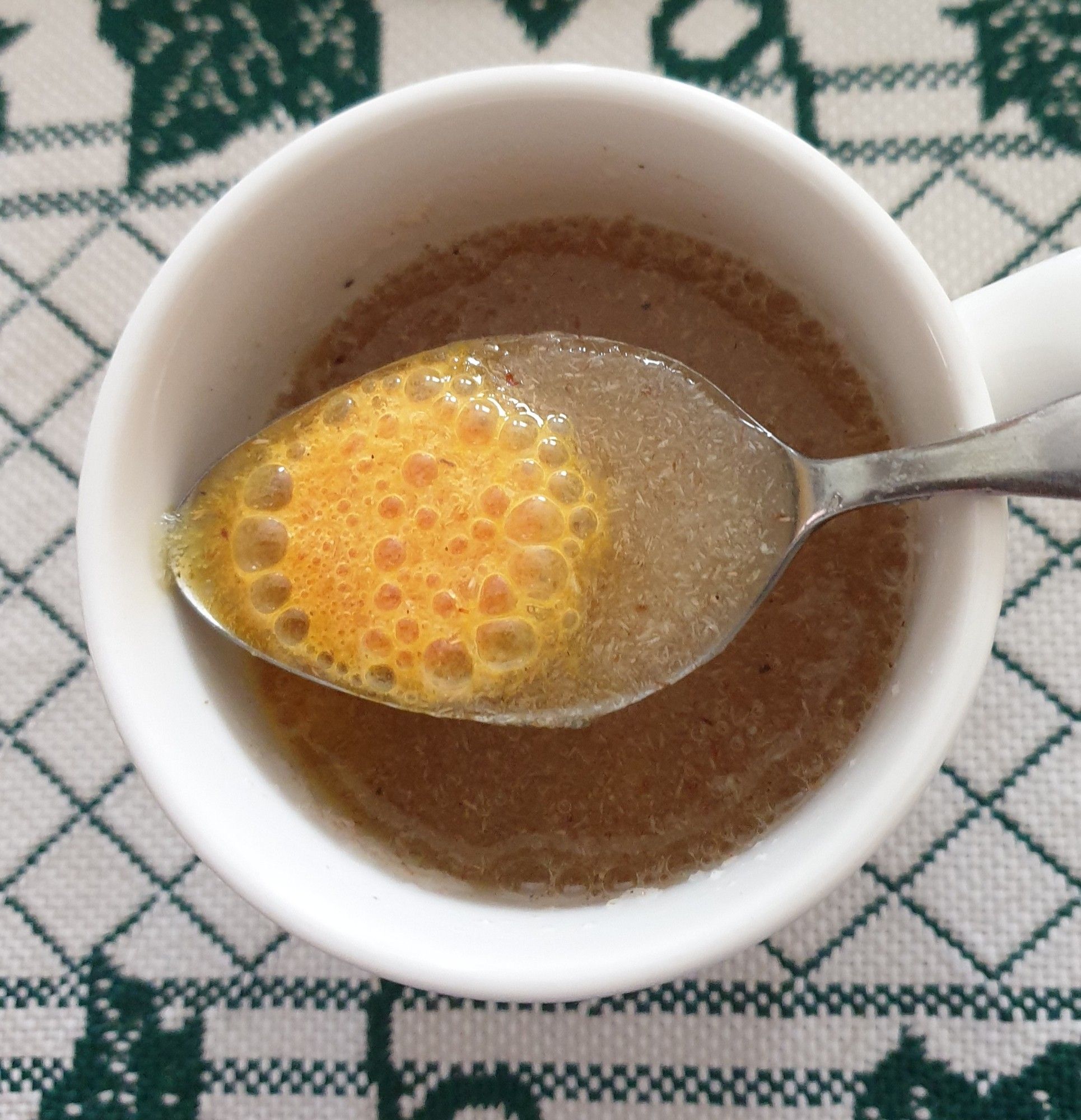 Mug of psyllium husk mixed with water on green and white cloth. Dessertspoon resting on top with gently fizzing orange vitamin C tablet