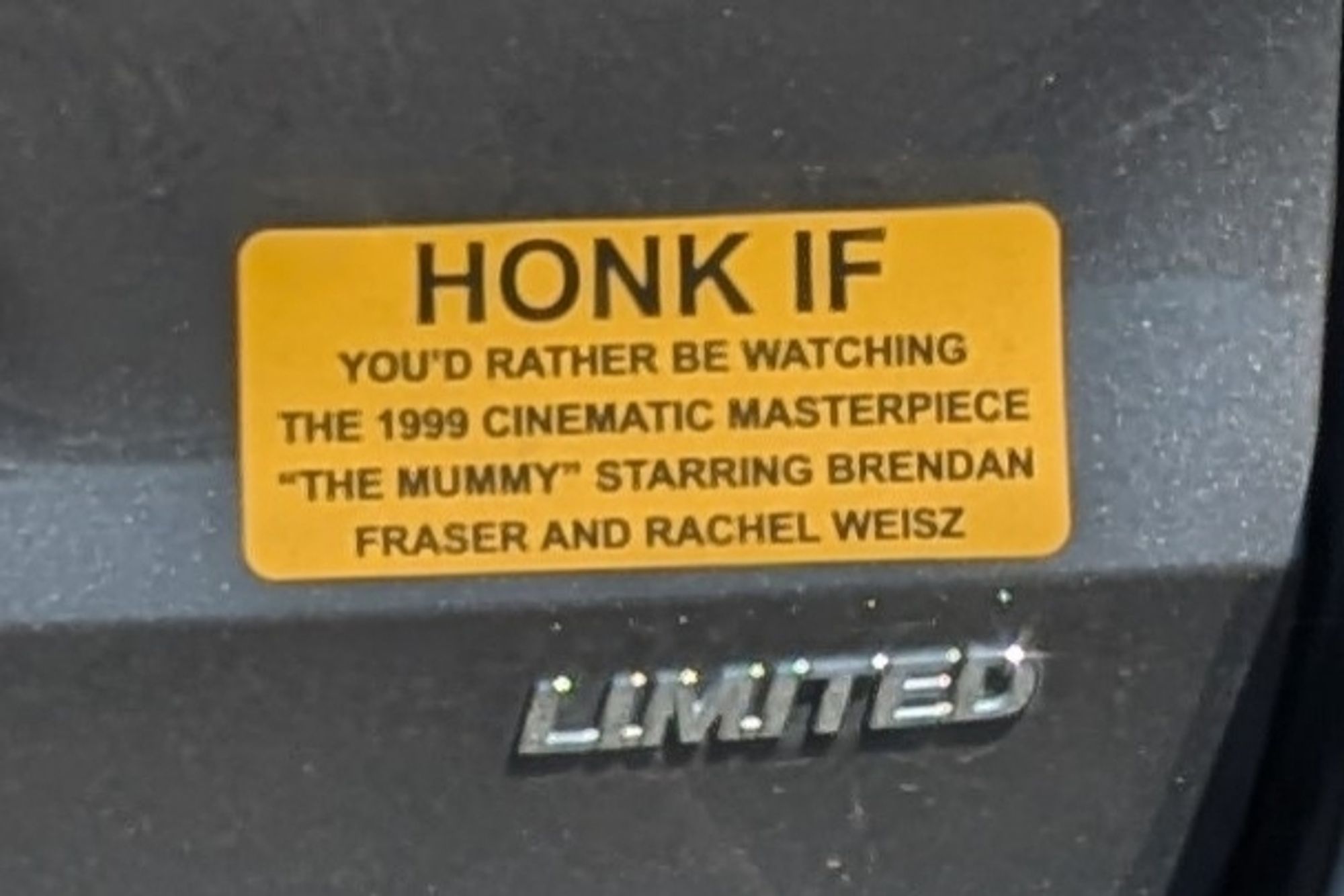 Bumper sticker that reads "HONK IF YOU'D RATHER BE WATCHING THE 1999 CINEMATIC MASTERPIECE "THE MUMMY" STARRING BRENDAN FRASER AND RACHEL WEISZ"