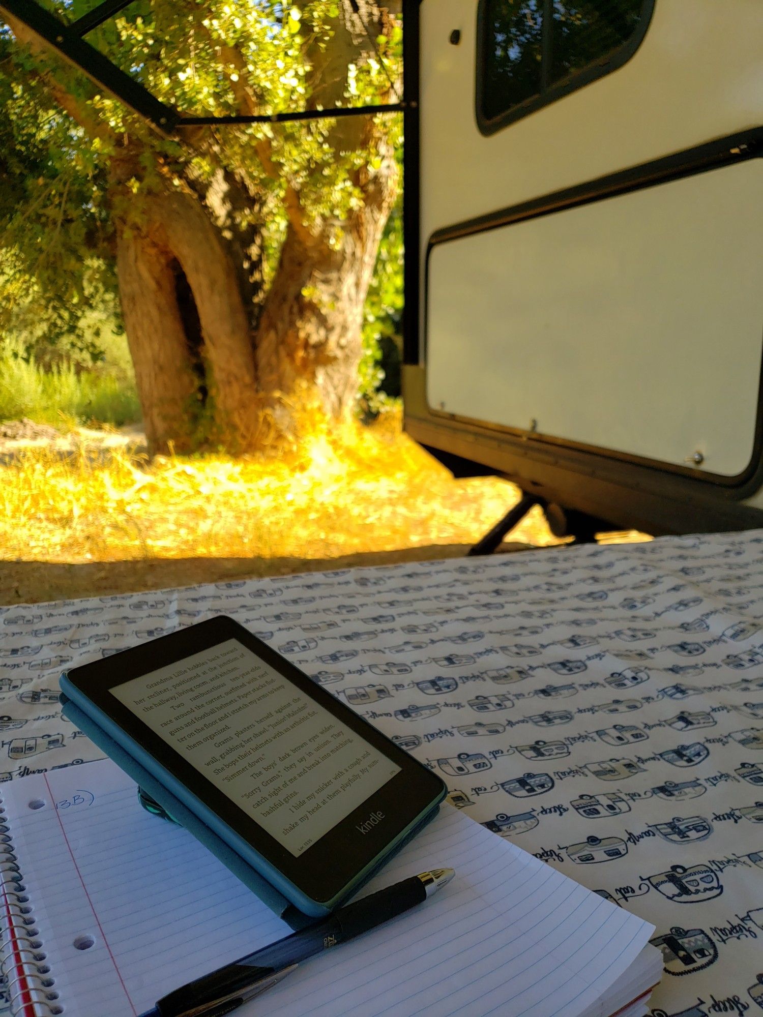 Kindle and notepad on a picnic table next to a camper