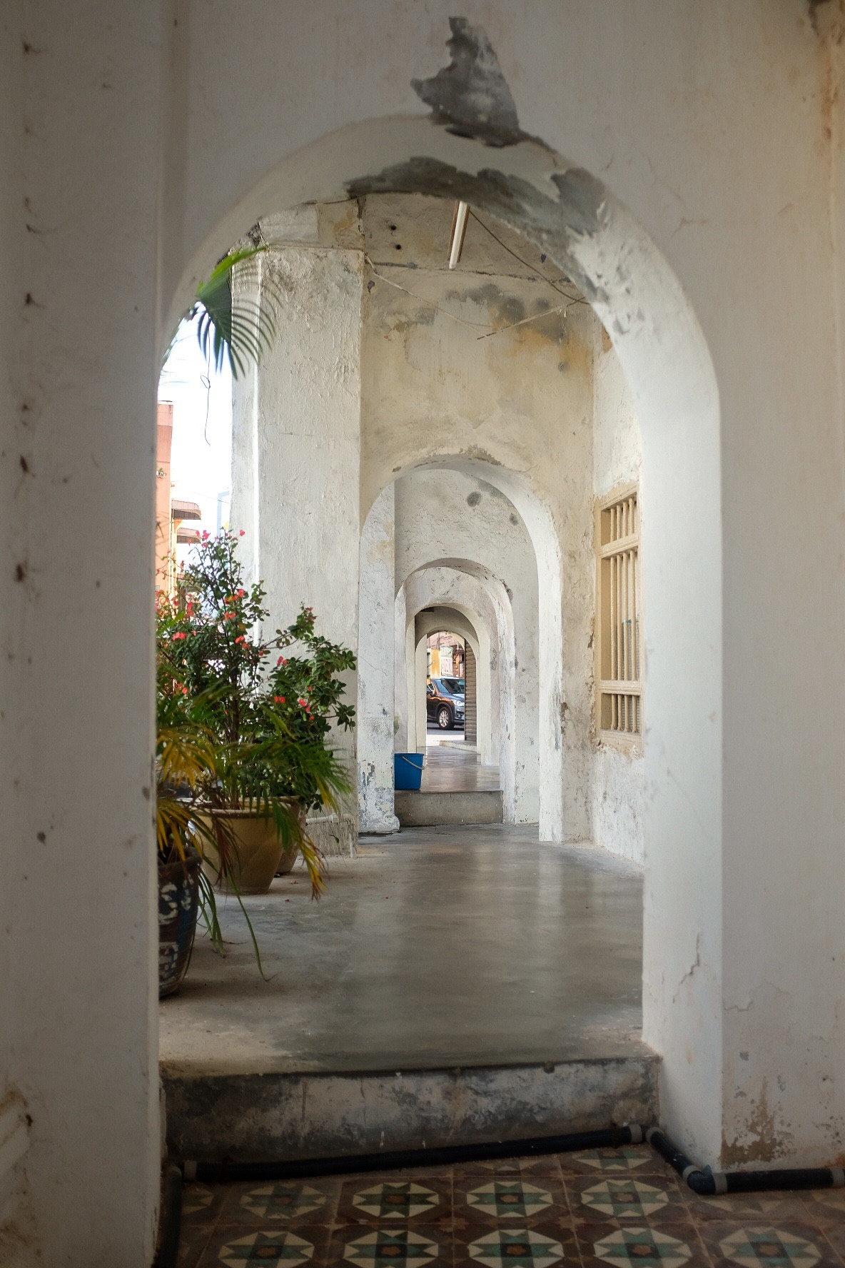 A sidewalk outside storefronts sheltered by domed passageways. In the foreground, Portuguese tiles in one section of the ground, typical of certain Chinese-diaspora areas in Southeast Asia.