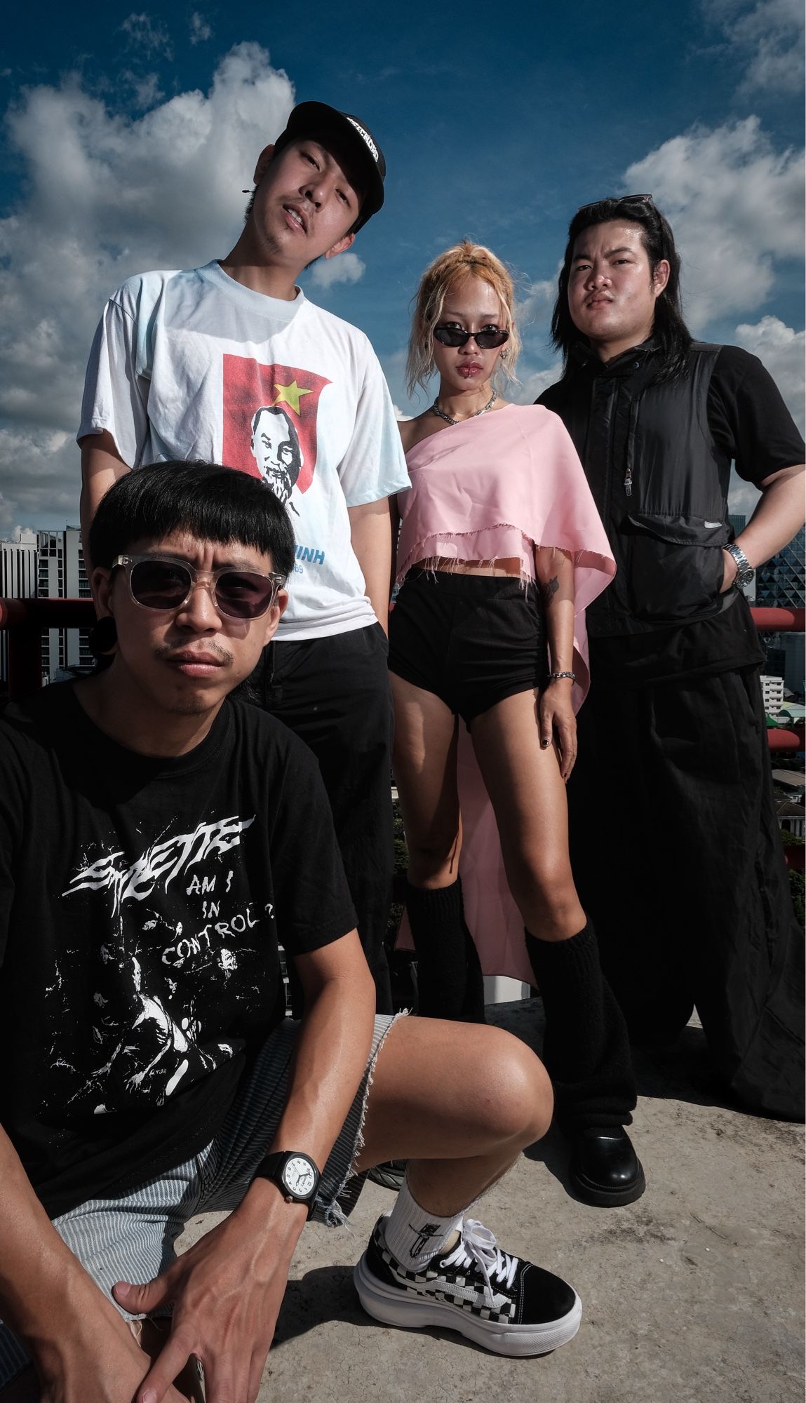 3 young Thai men and 1 young woman stand on a rooftop. 1 man is crouching.