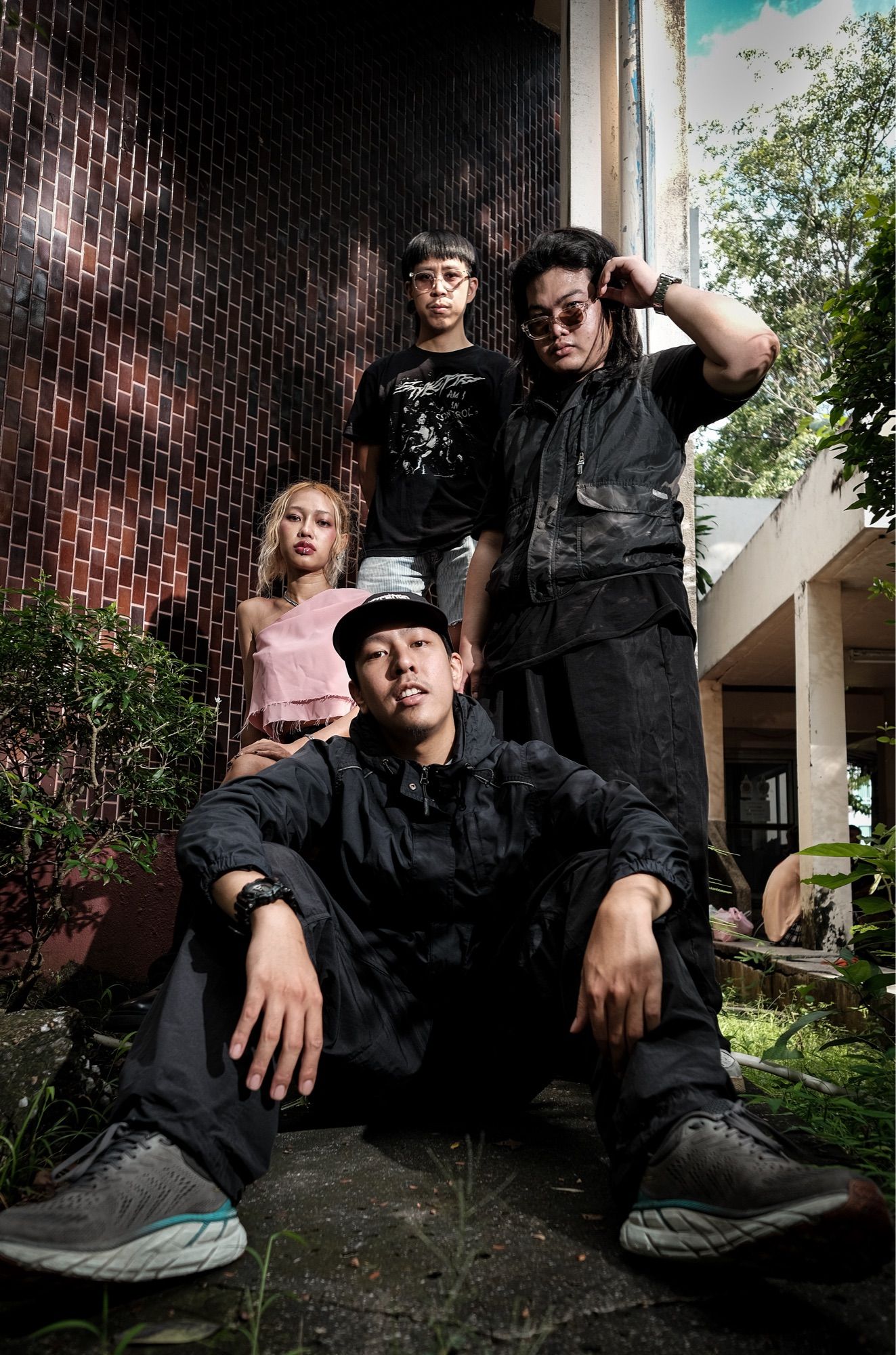 3 young Thai men and 1 young woman sit in the yard of a building inside a park.