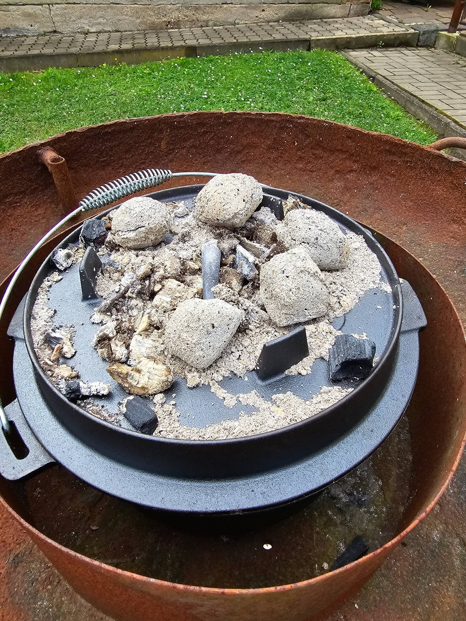 Gusseisener Topf bedeckt mit Grillbriketts - ein sog
 Dutch Oven