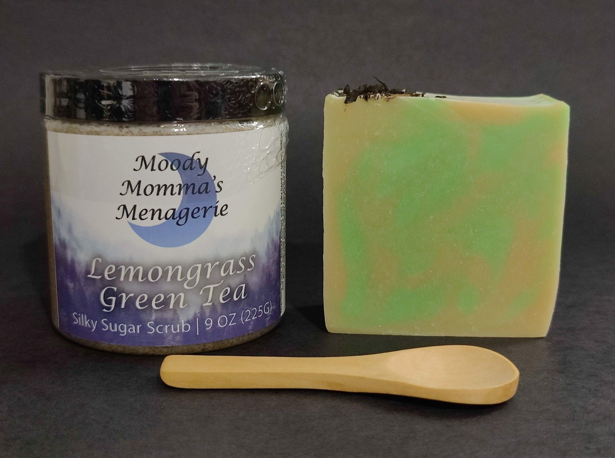 A jar of Lemongrass Green Tea emulsified sugar scrub sitting next to a bar of green and gold Lemongrass Green Tea soap with a small bamboo spoon in front