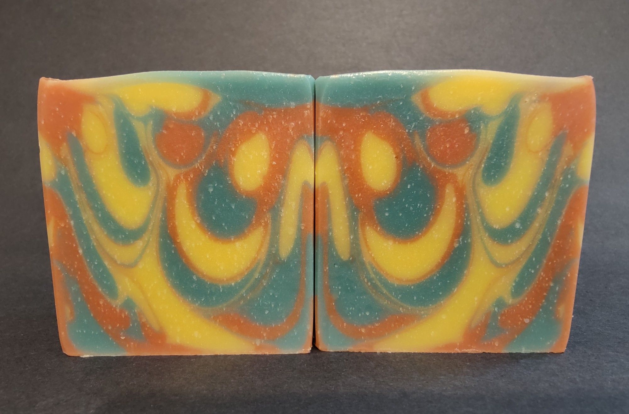 Two bars of green, yellow and orange soaps sitting next to each other showing an inkblot like design