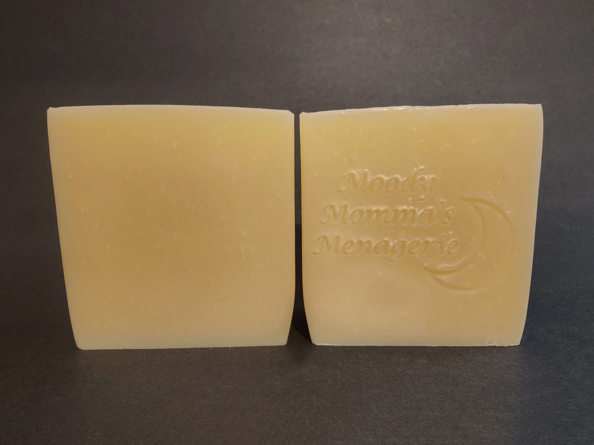 Two bars of creamy white soaps sitting side by side. The right bar is stamped with "Moody Momma's Menagerie" and a crescent moon