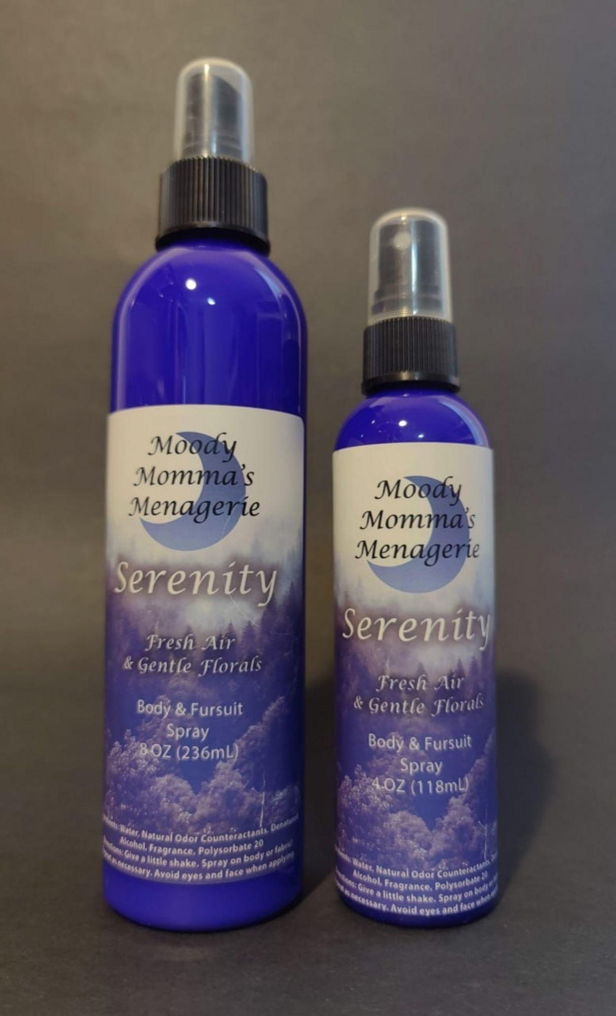 An 8 ounce blue bottle and a 4 ounce blue bottle of body/fabric spray in the fragrance Serenity. The fragrance notes are Fresh Air & Gentle Florals.