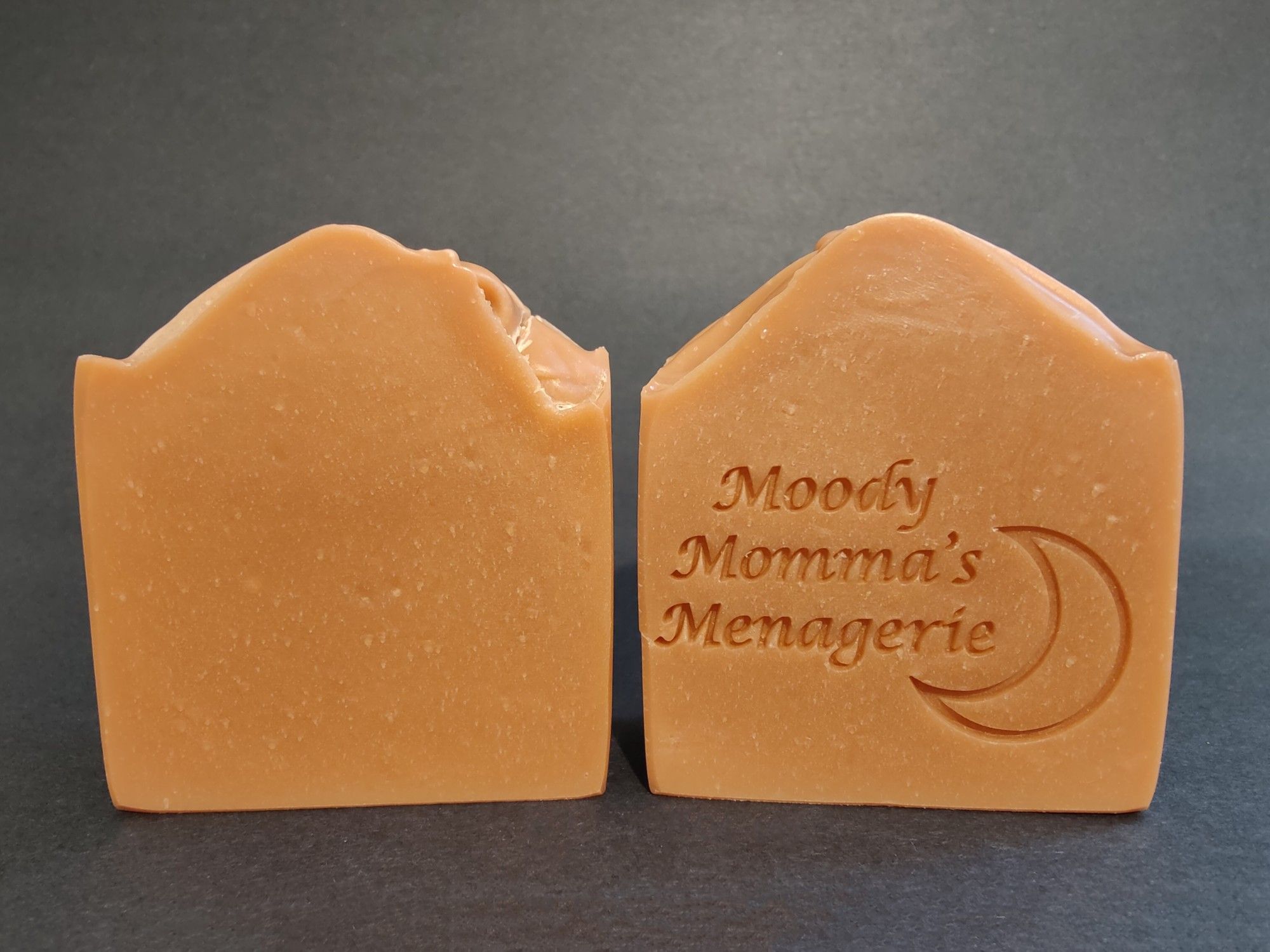 Two bars of coppery soaps sitting next to each other. The right is stamped with "Moody Momma's Menagerie" and a crescent moon