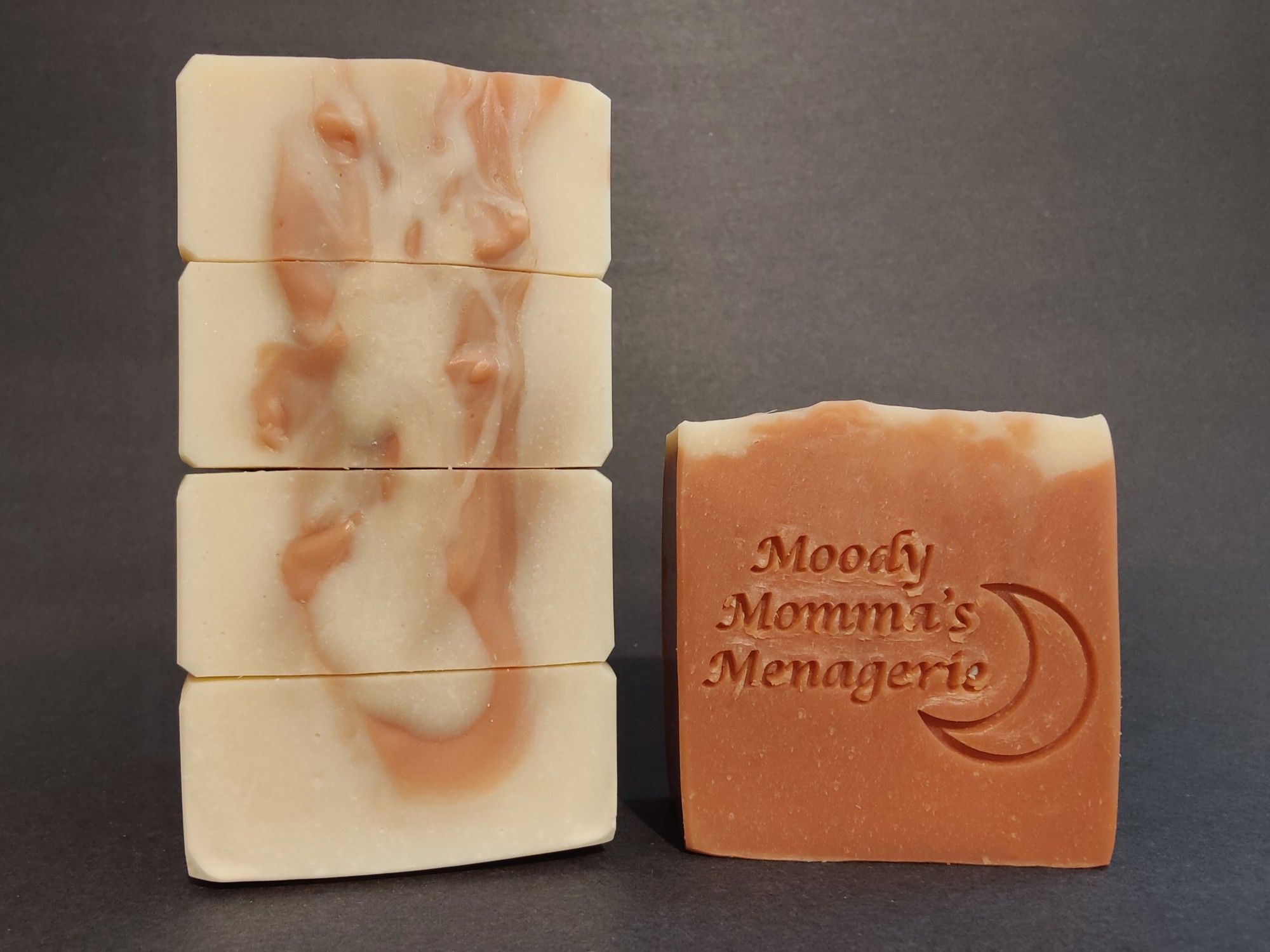 On the left are four soaps stacked on their side to show the top texture, reminiscent of the sun's corona. On the right is a single bar with a crescent moon and "Moody Momma's Menagerie" stamped into it