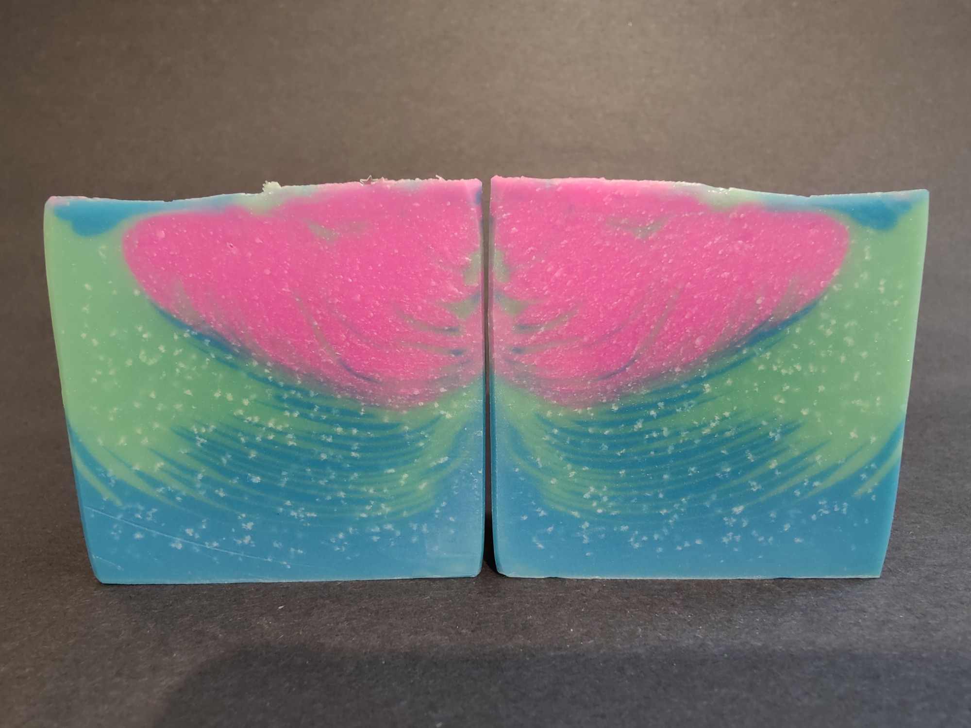 Two bars of pink, blue and green soaps sitting side by side with a feathered pattern