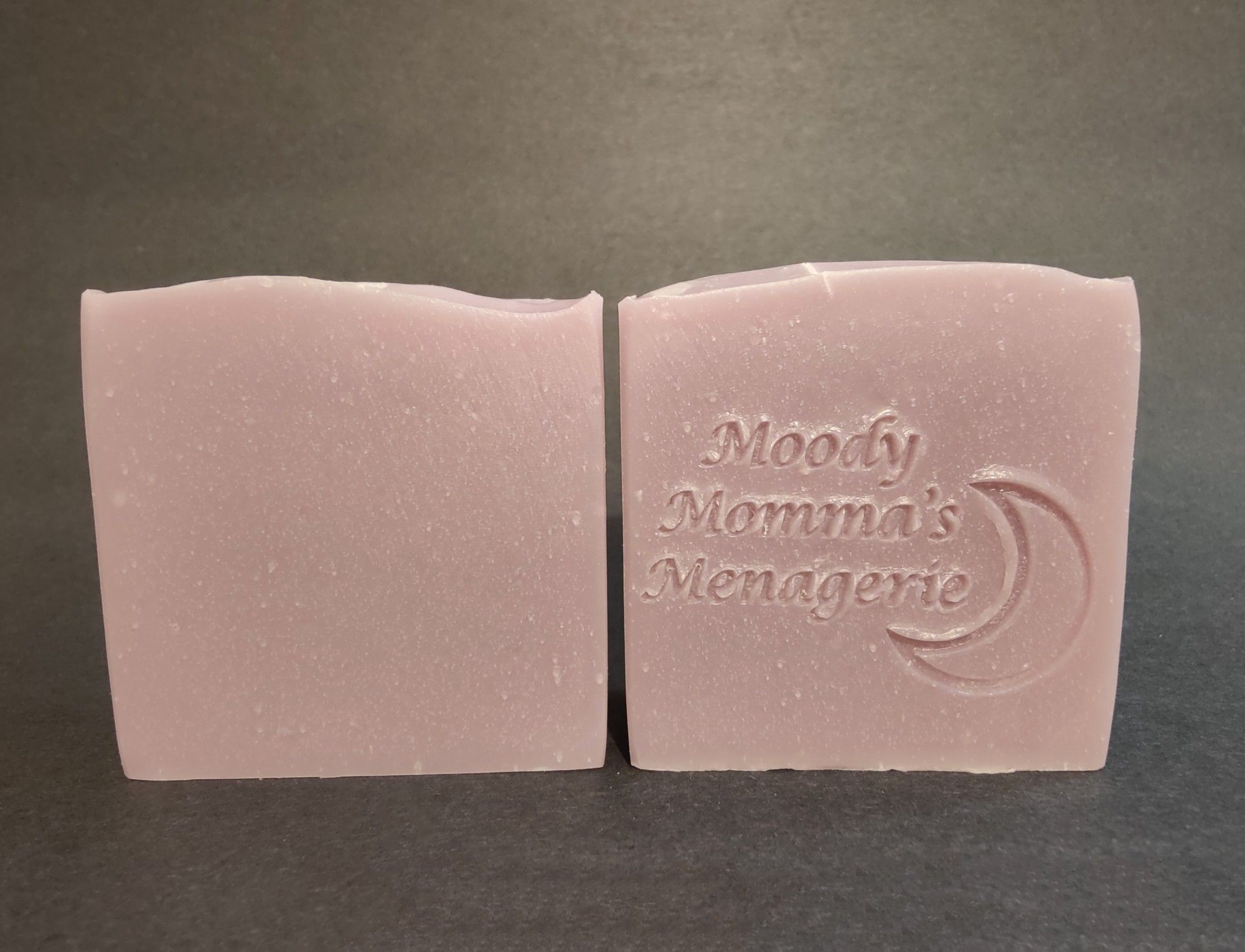 Two bars of lilac colored soaps sitting side by side. The right bar is stamped with "Moody Momma's Menagerie" and a crescent moon