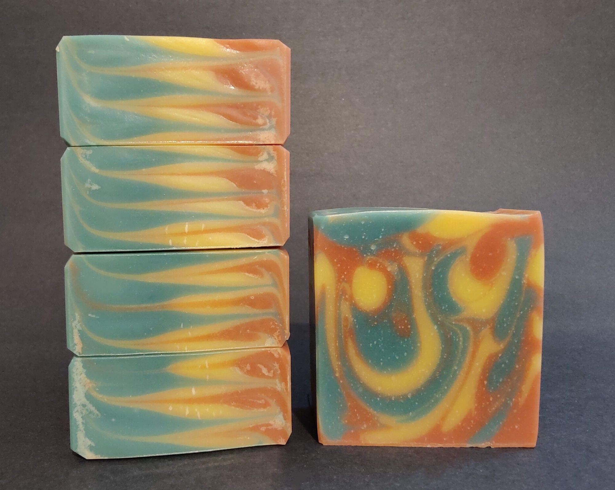 On the left are four bars of green, yellow and orange soaps stacked on their side to show the top swirl detail. On the right is a single bar of the green, yellow and orange soap