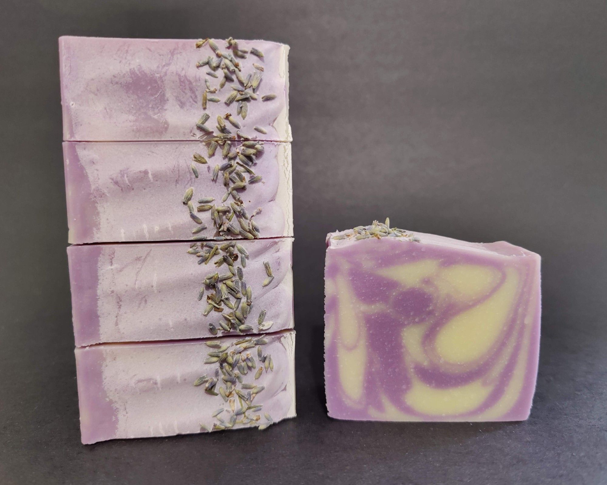 On the left are four lavender soaps stacked on their side to show the top detail with lavender buds sprinkled along one side. On the right is a single bar of purple and white lavender soap