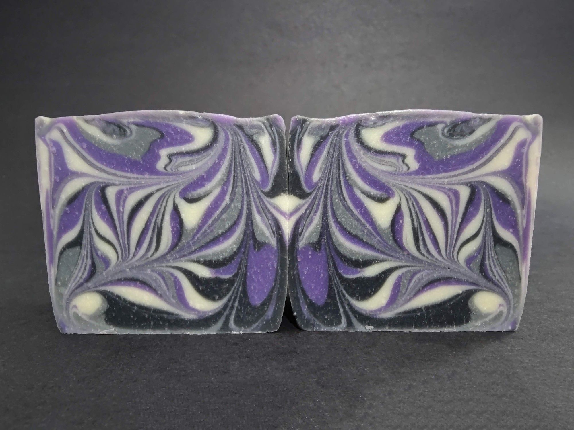 Two bars of black, grey, white and purple soaps with a swirled design. These soaps are the Ace Pride swirl design and scented in a cherry limeade fragrance