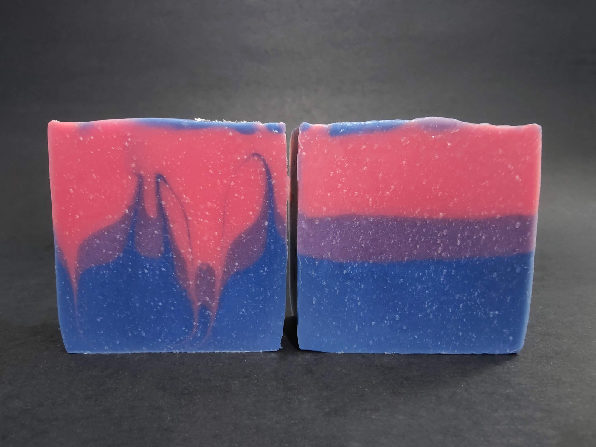 Two soaps colored with the Bisexual Pride flag colors, pink, purple and blue. The left has a swirl design and the right is layered