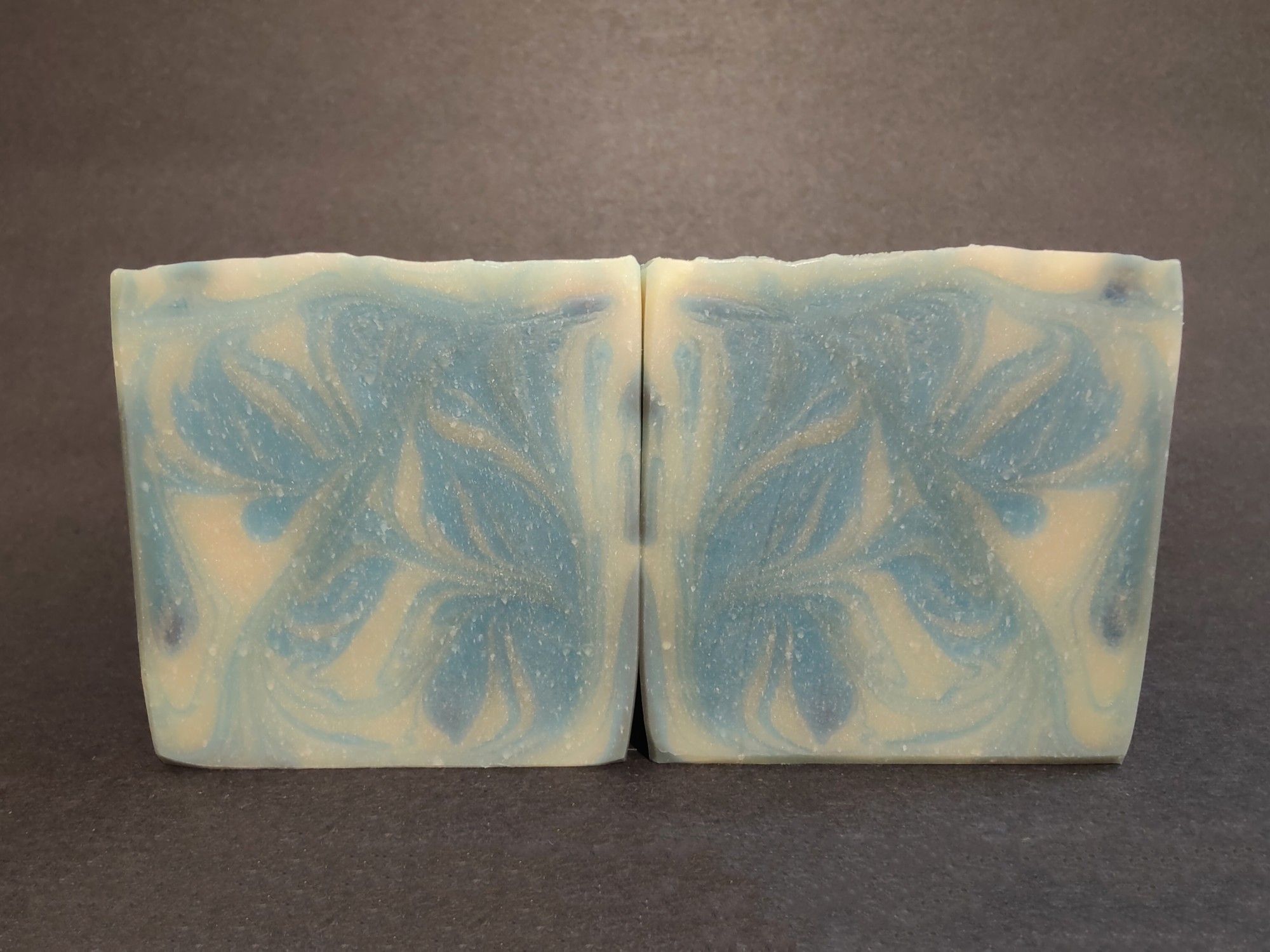 Two blue and white soaps are sitting side by side to show their swirls