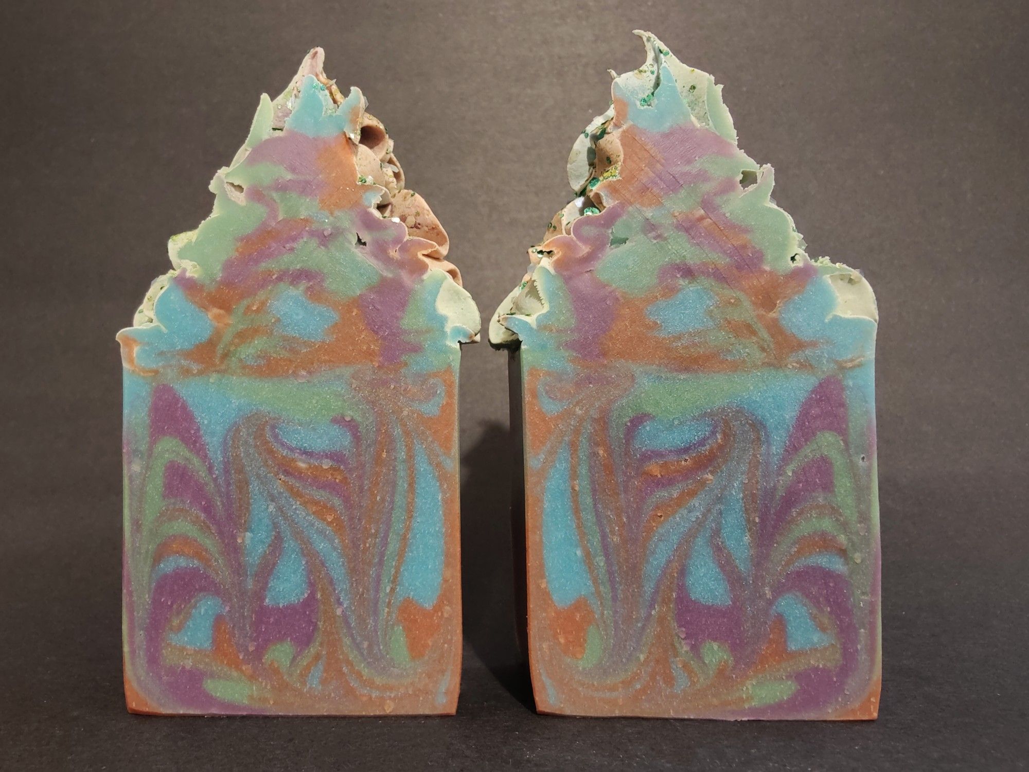 Two large bars of swirled purple, green, blue and brown colored soaps with "frosted" tops and biodegradable plant based glitter