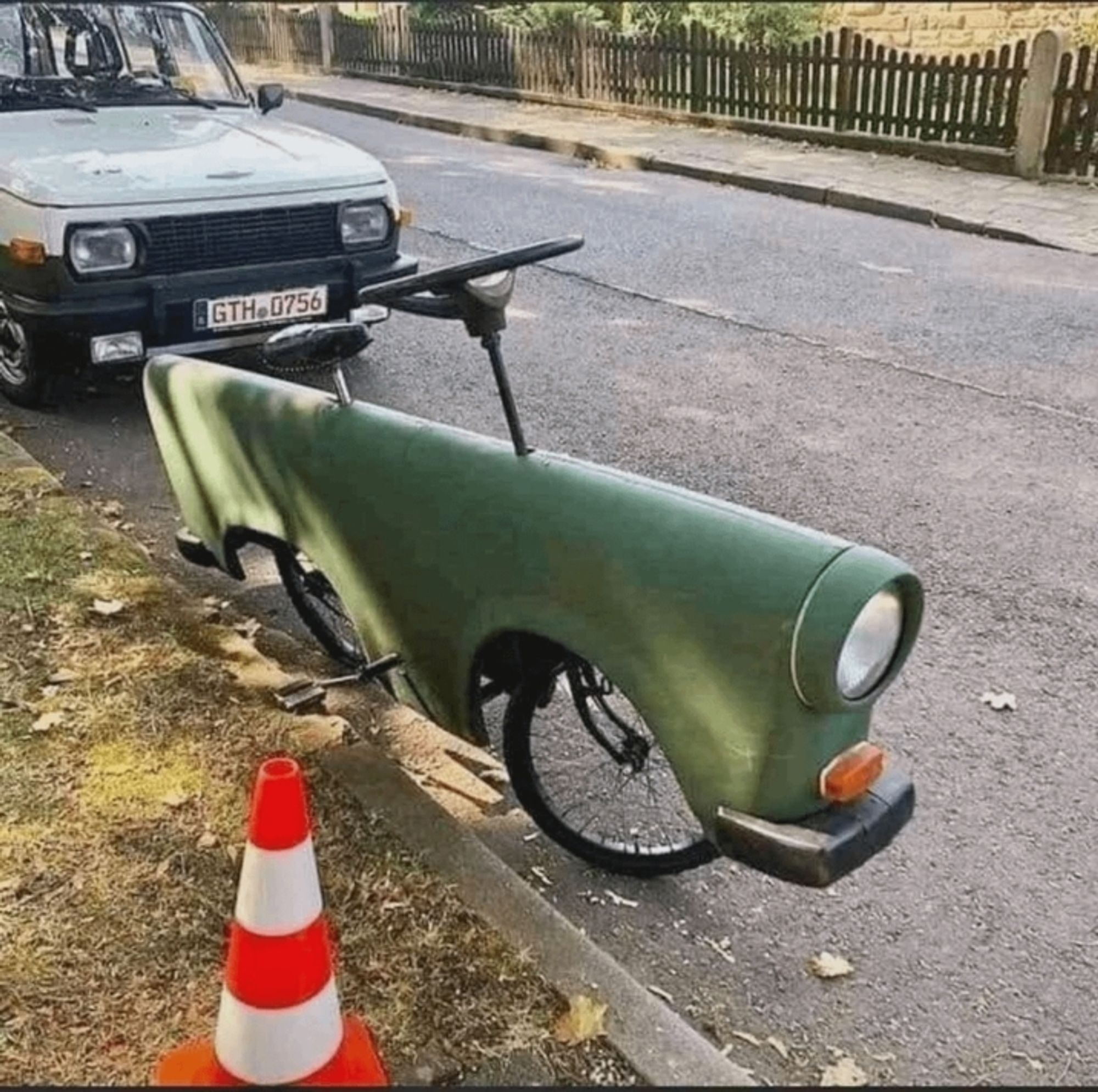 A green metal vehicle body with a bicycle under it , one headlight and blinker