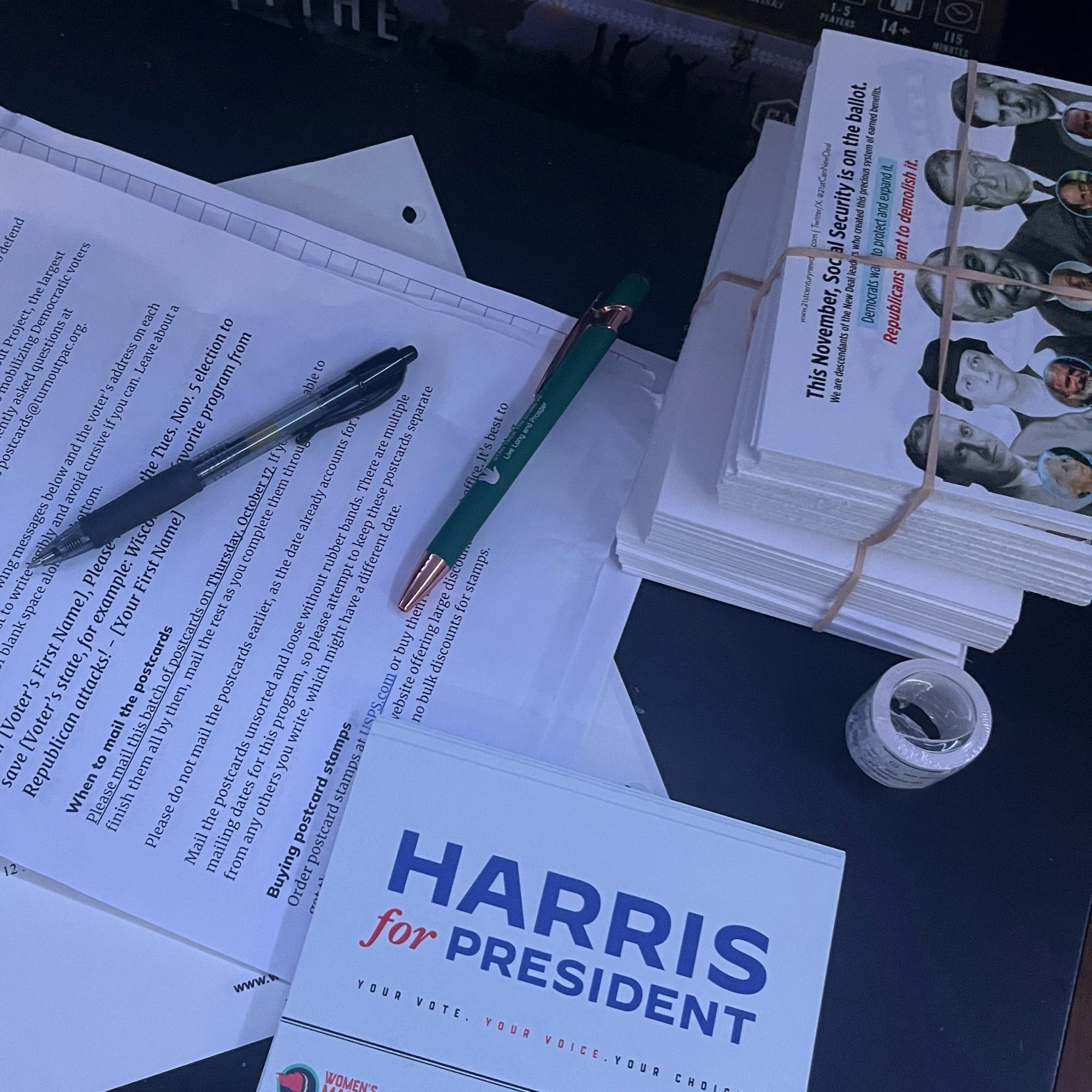 A picture of a tv desk with a stack of postcards, pens, and instruction letter with a roll of stamps next to them