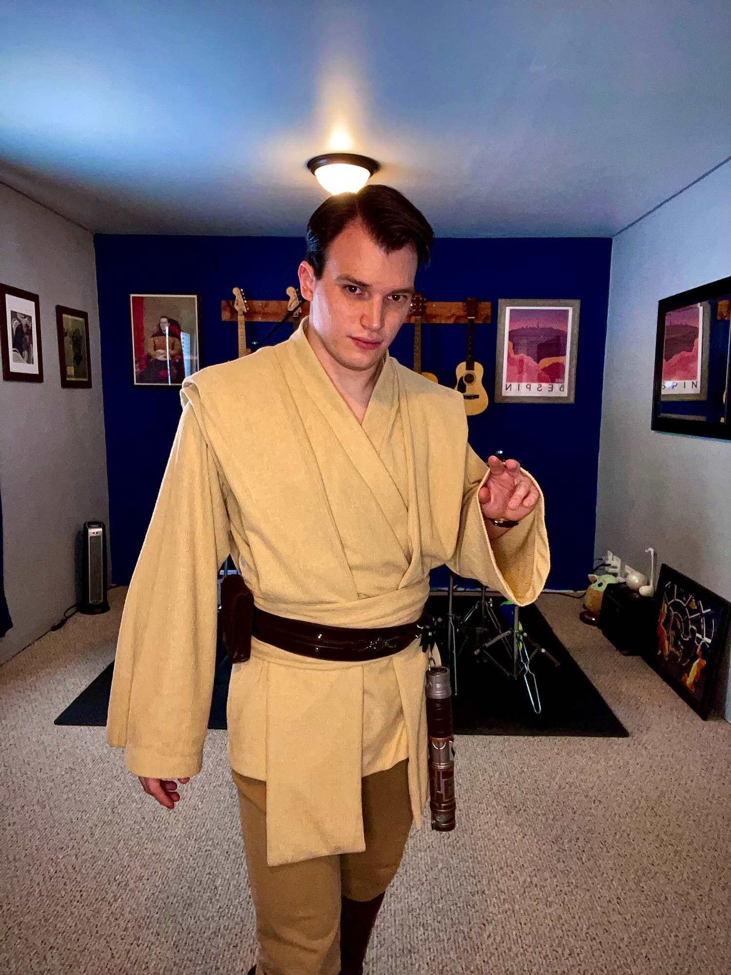 A photo of Colton dressed in Jedi robes from Star Wars Galaxy's Edge featuring a lightsaber in the Elemental Nature style from Savi's. His expression is a poor imitation of a smolder