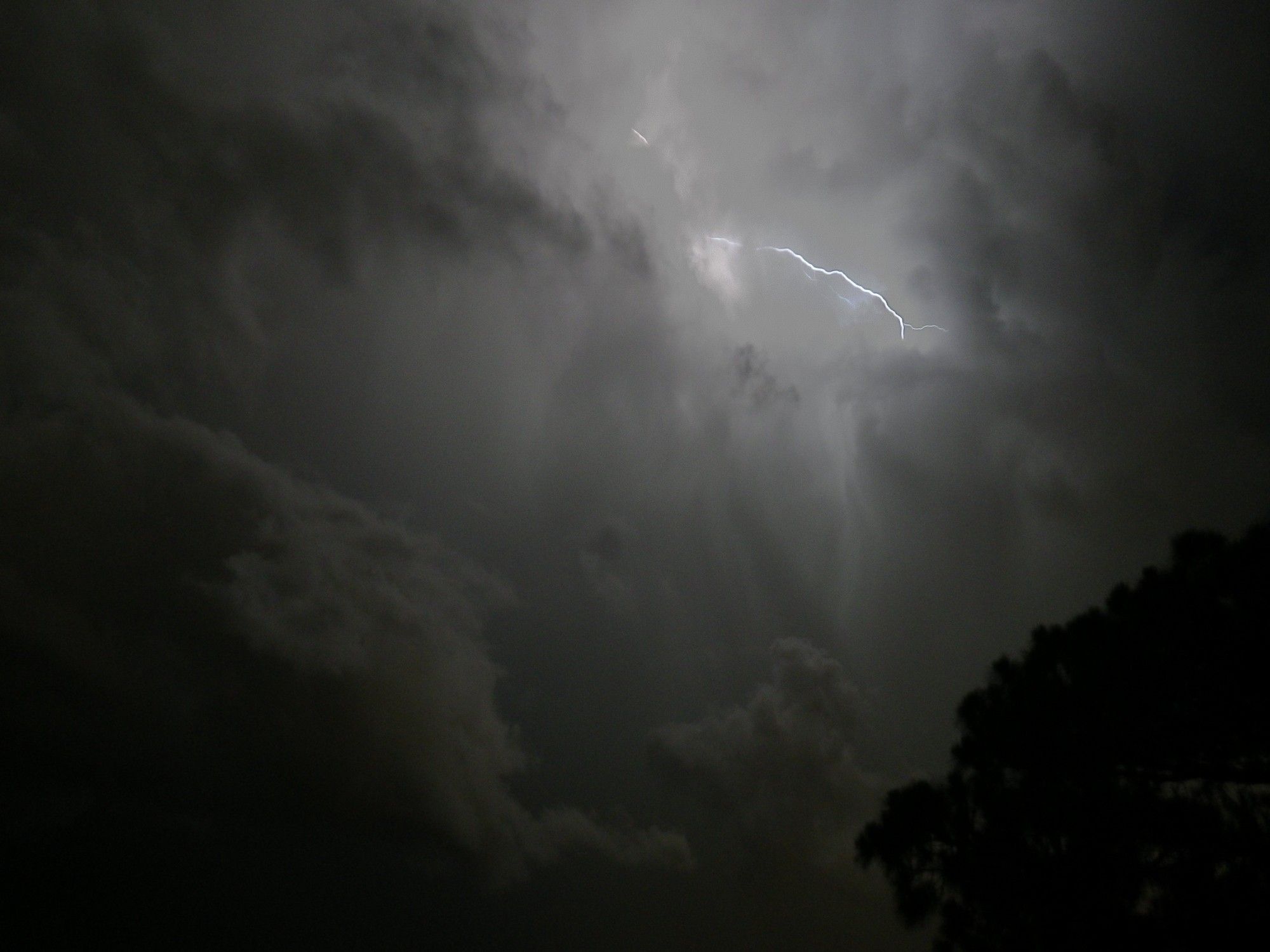 A very dark and somewhat blurry image of grey storm clouds, illuminated by lightning peeking through a few clouds. Very spooky atmosphere.