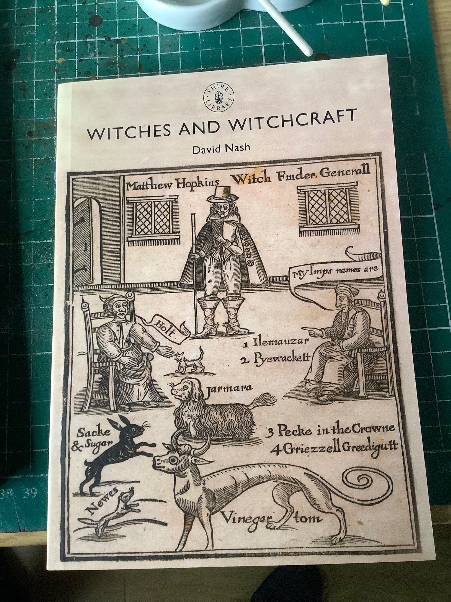 Phot of a Shire Library series book cover entitled “Witches and Witchcraft”. The cover depicts Matthew Hopkins as the Witch finder General surrounded my witches and familiars.