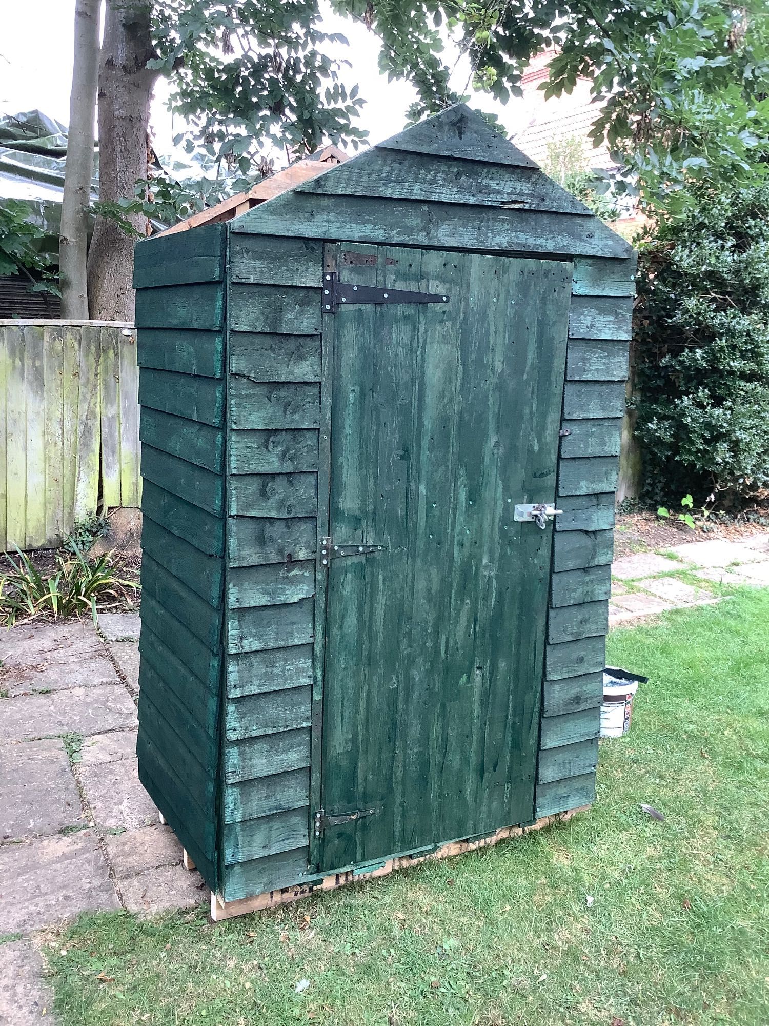 A very small timber tool shed, painted green.