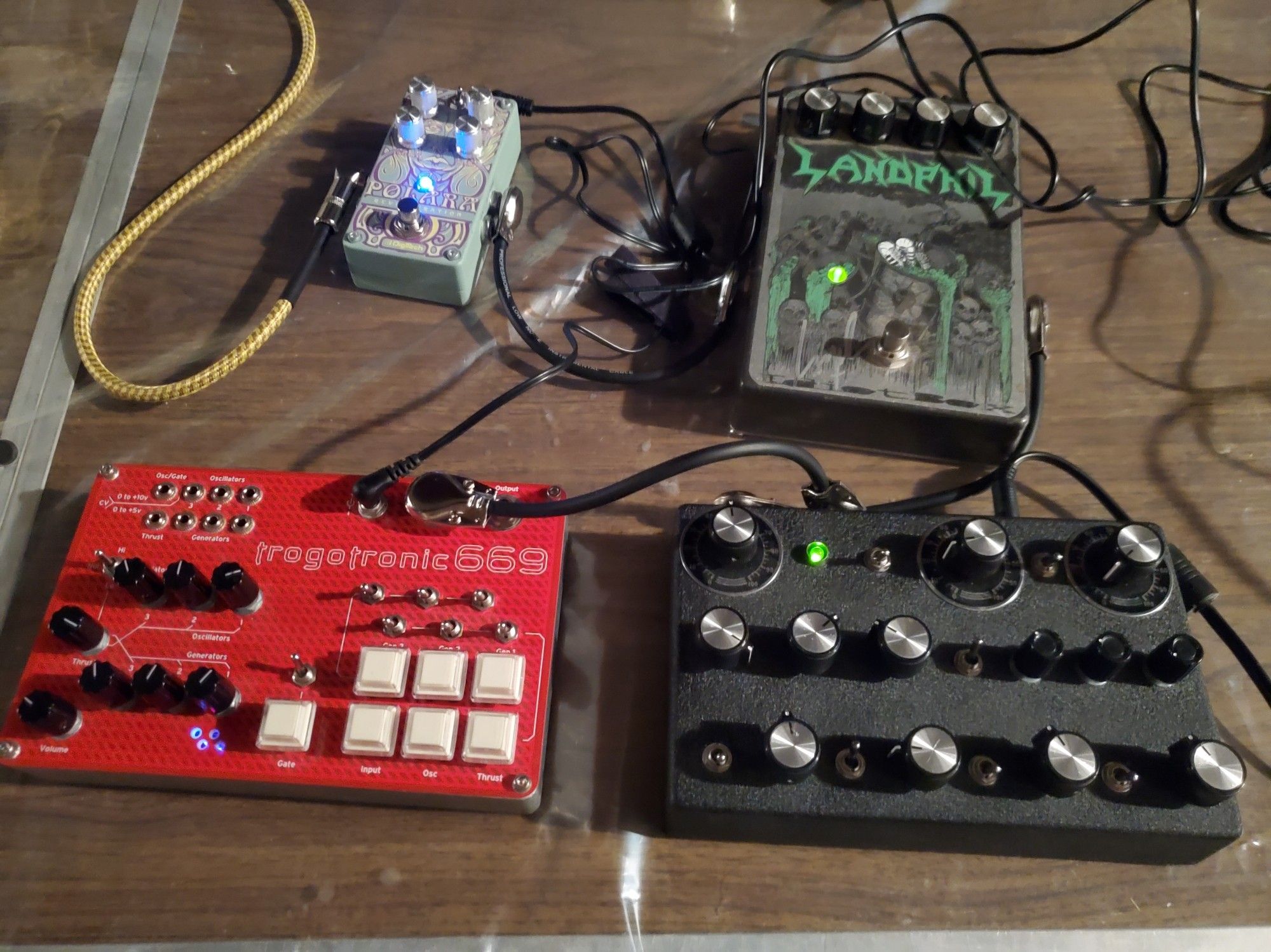 Closeup of a Trogotronic 669cv Boss Hog MiniSynth chained into a JMT Synth DNVO-1 Desktop Synthesizer chained into an Idiotbox Landphil pedal and a Digitech Polara reverb.