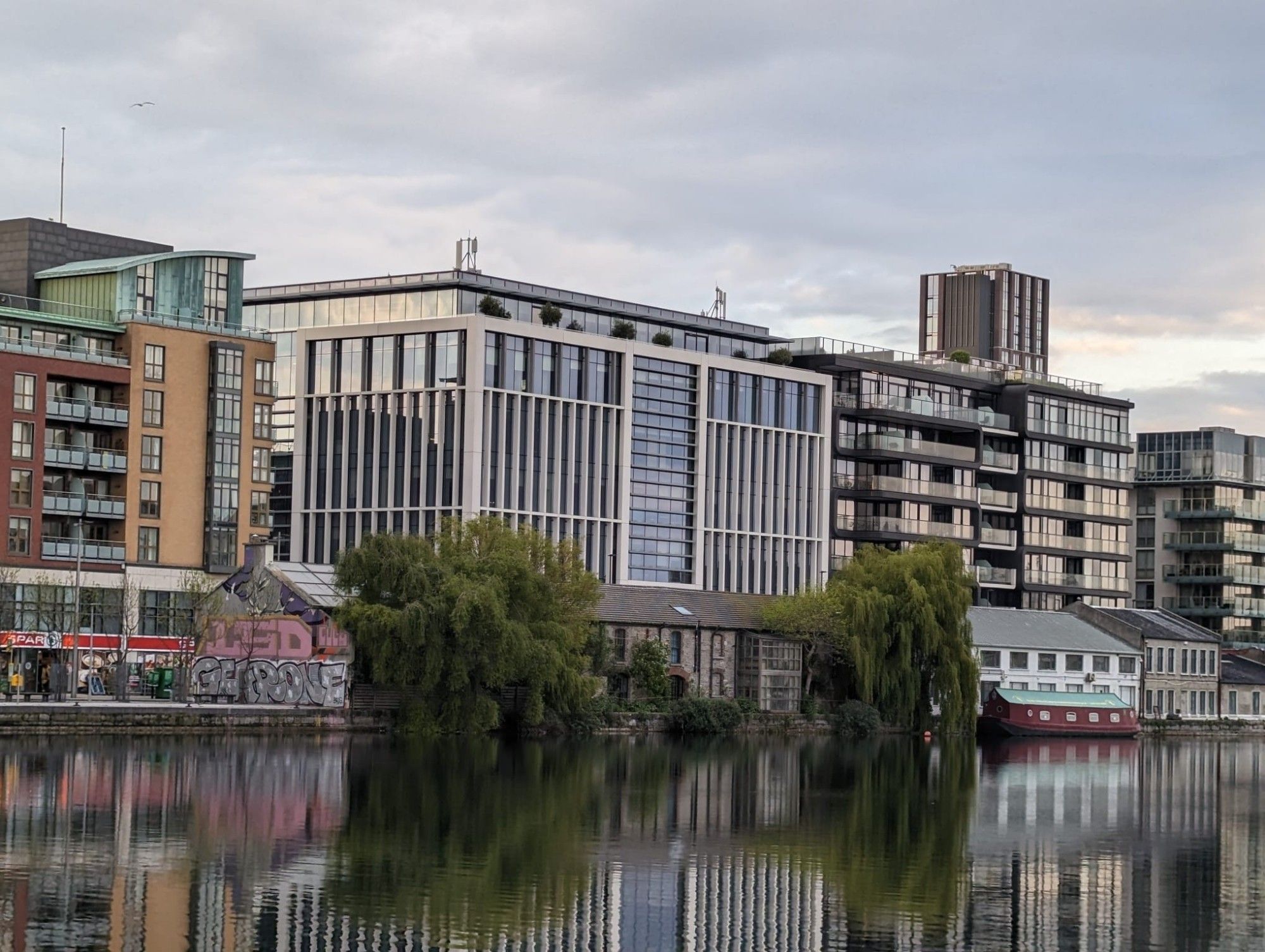 Grey, ugly city scape by the waterfront. Steel and glass five-over-ones. A small row of old varyingly renovated warehouses. Two enormous willows (I think) are touching the water in front of these old warehouses. It's very pretty, and makes the whole image less horrible