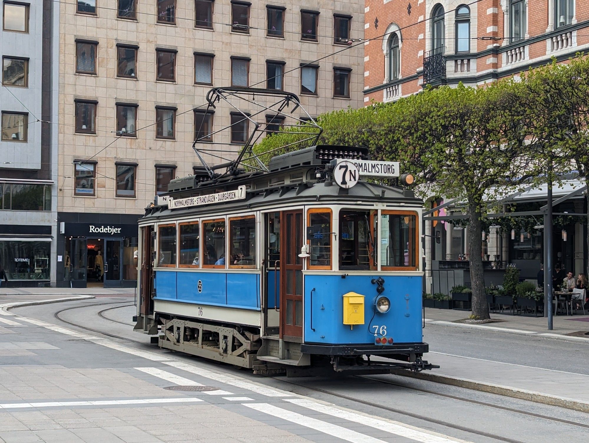 An old tiny (1920's?) tram single carriage, blue, white trip, wood interior. 7n code. On a tidy street with clipped trees behind