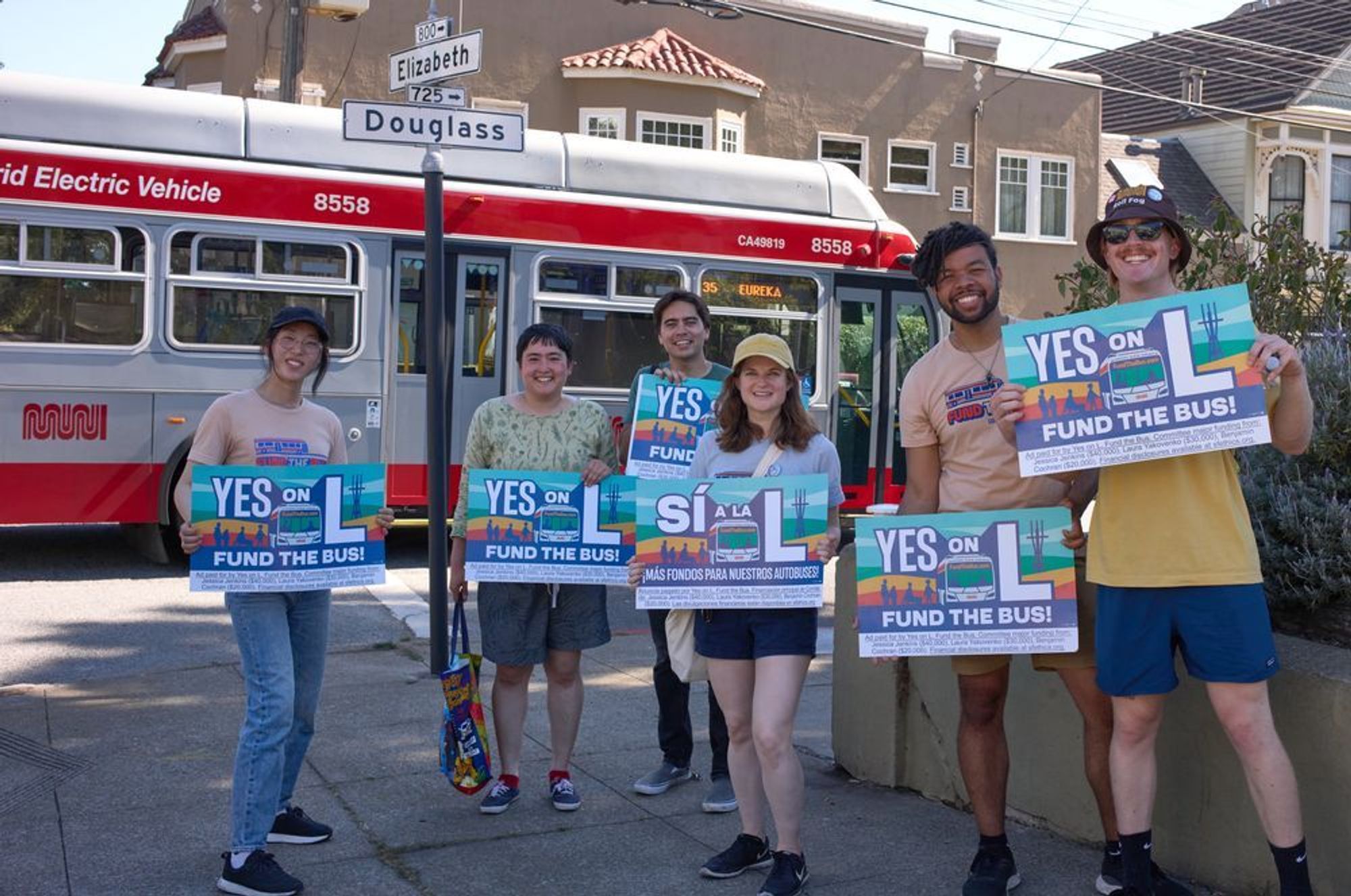 Six volunteers holding Yes on L window signs at the corner of Elizabeth and Douglass with a 35 Eureka bus in the background