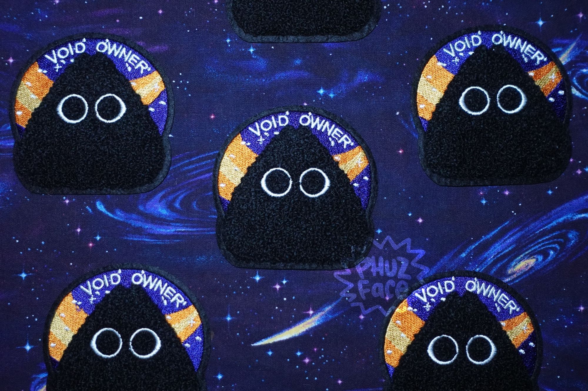 Several void owner patches laid out in a five pointed upright starlike pattern on a dark purple and blue cosmic tablecloth.