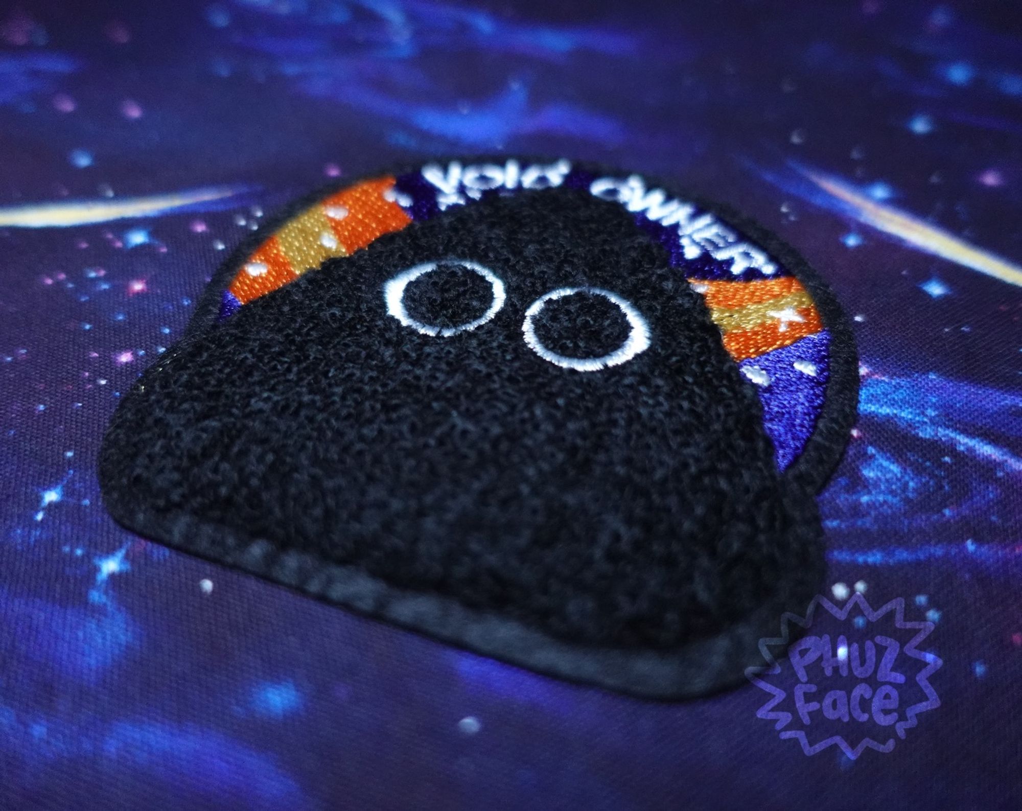 Tiltshift angle photo of a Void Owner patch on a dark purple and blue cosmic tablecloth.