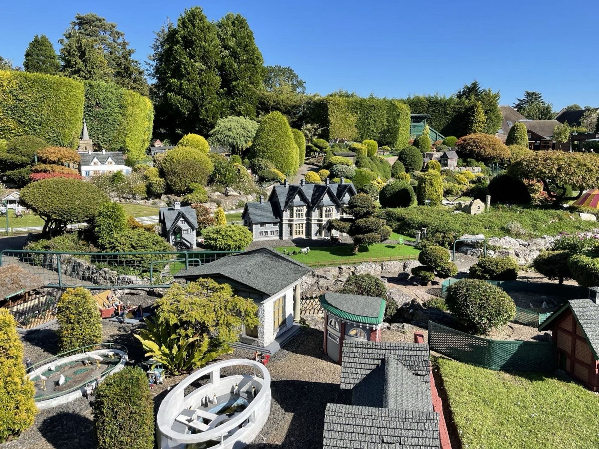 A model village surrounded by lawn, trees and hedges.