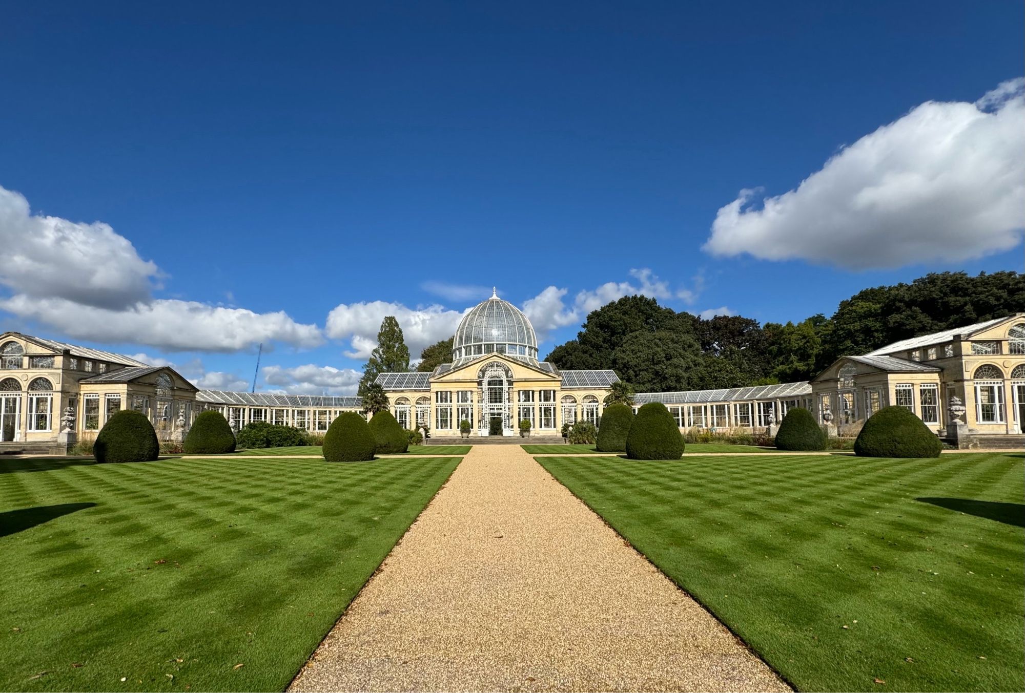 A path through a lawn to a large domed conservatory with curving wings.