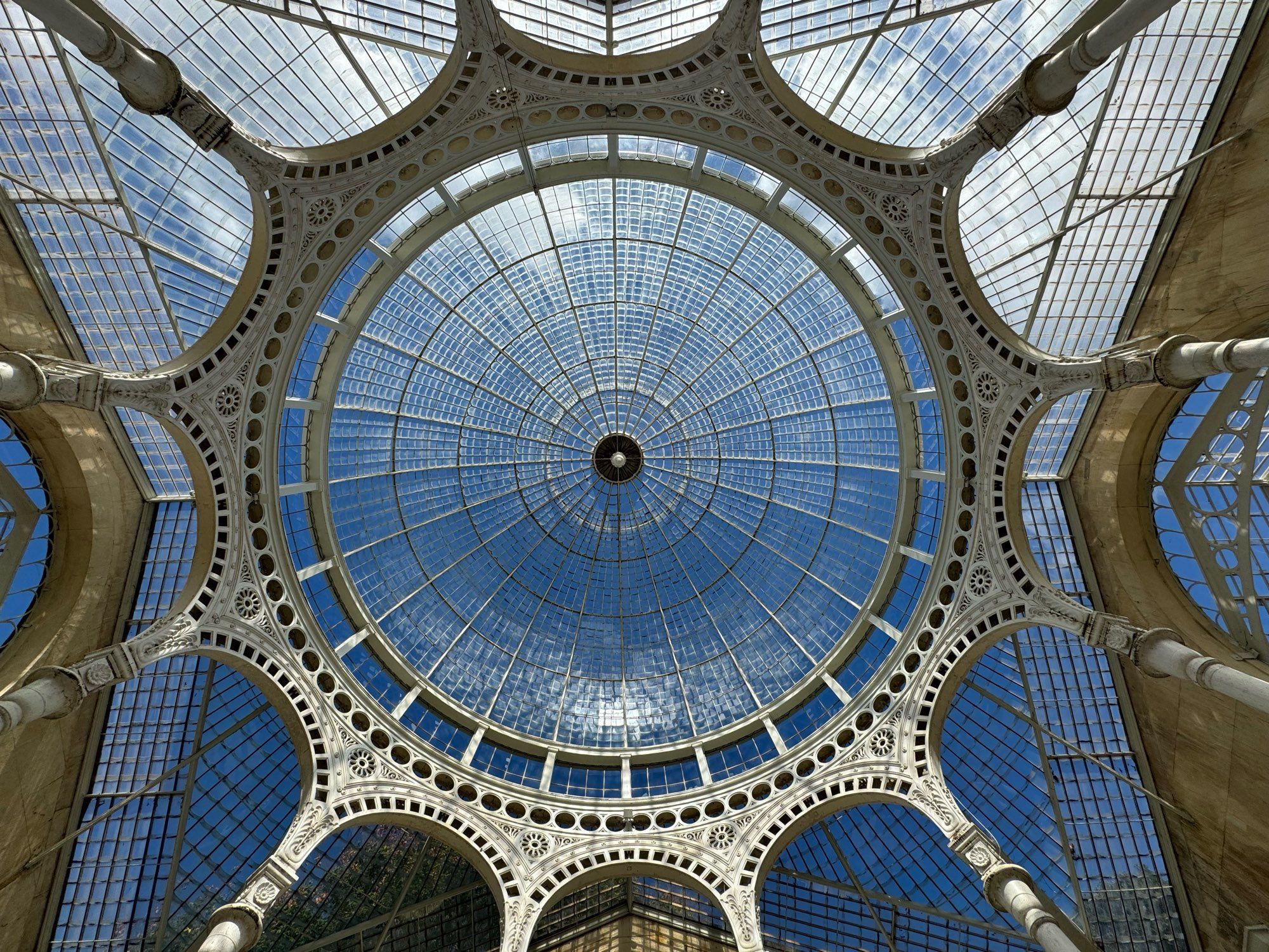 A view upwards into a large glass dome supported by ornate ironwork.