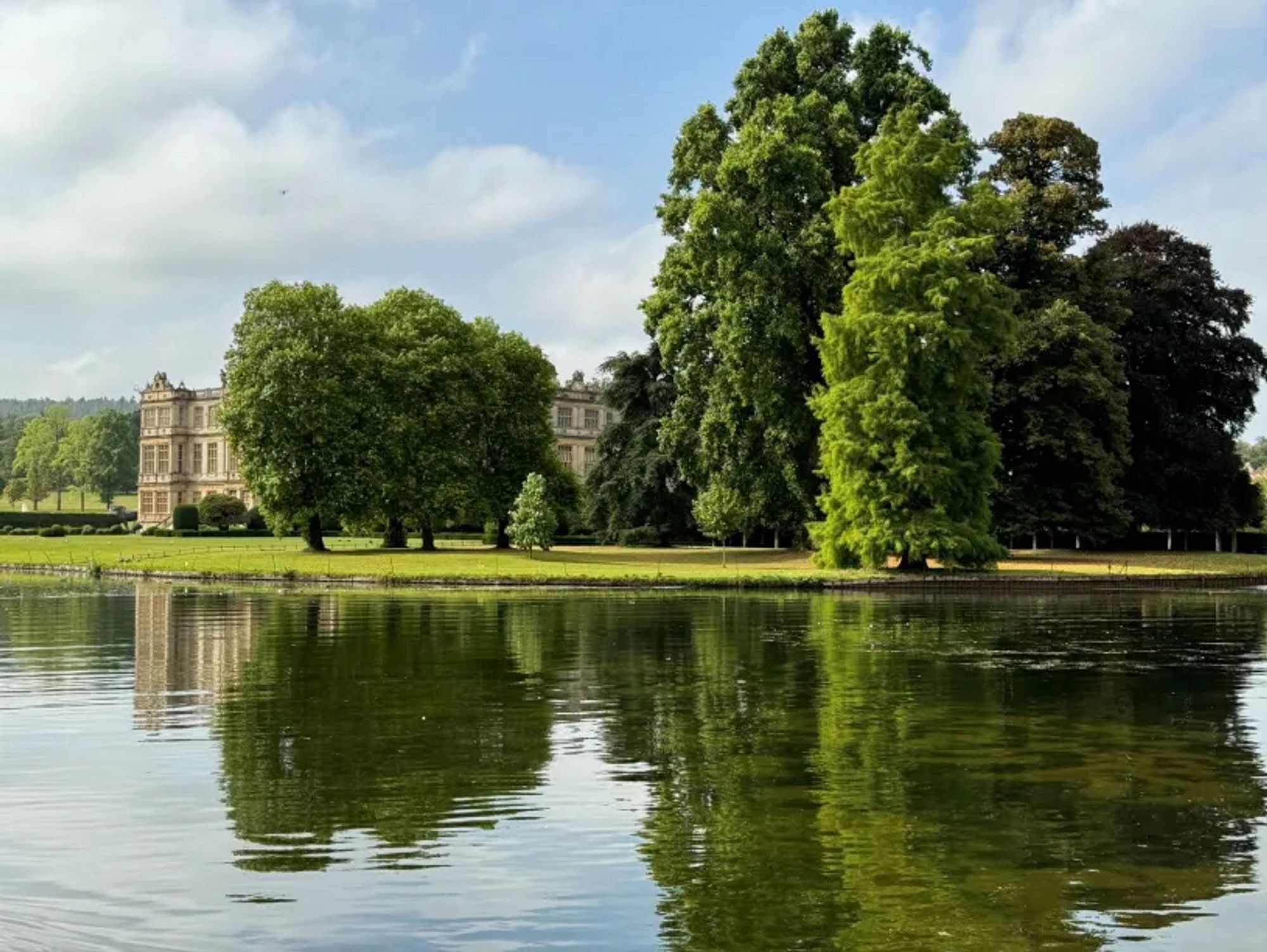 A large country house seen from a lake, with lawn in front and trees to the side.