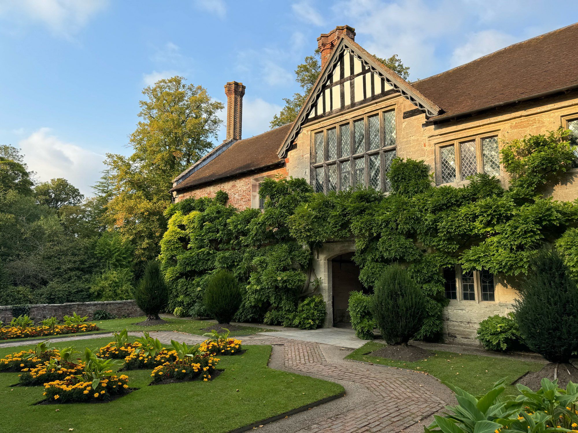 A formal courtyard garden, with geometric lawn and flower beds, and climbers covering most of the surrounding building.