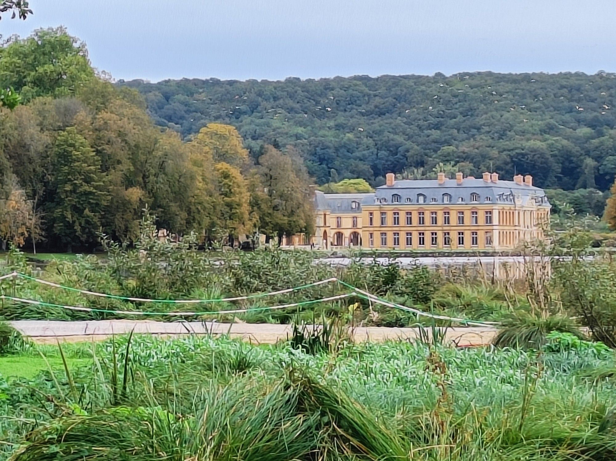 View of a stately home taken across its grounds with wooded hills in the background