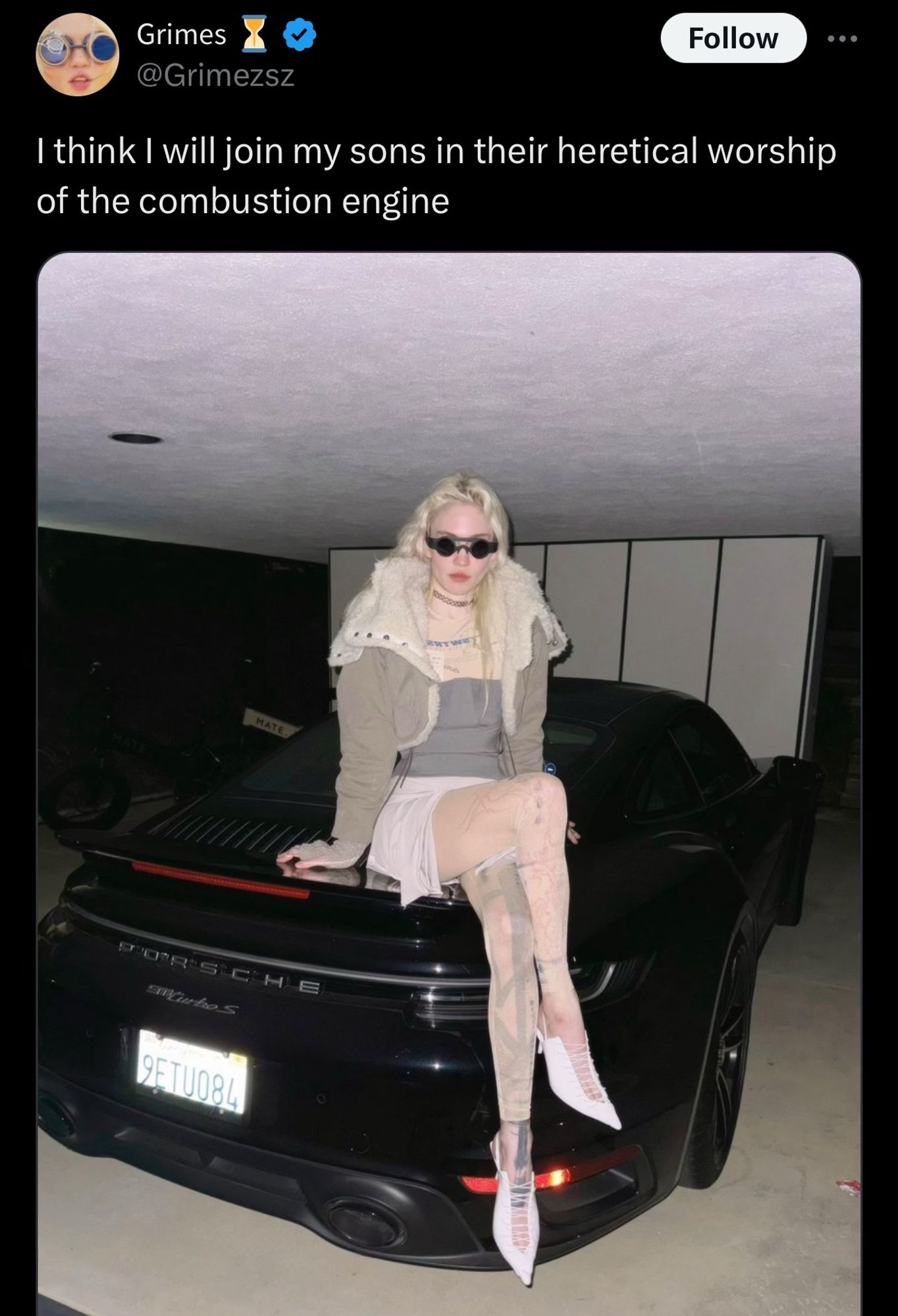 Tweet from Grime that reads: 
I think I will join my sons in their heretical worship of the combustion engine

It features a picture of her sitting on the back of a Porsche, with the license plate 9ETU084