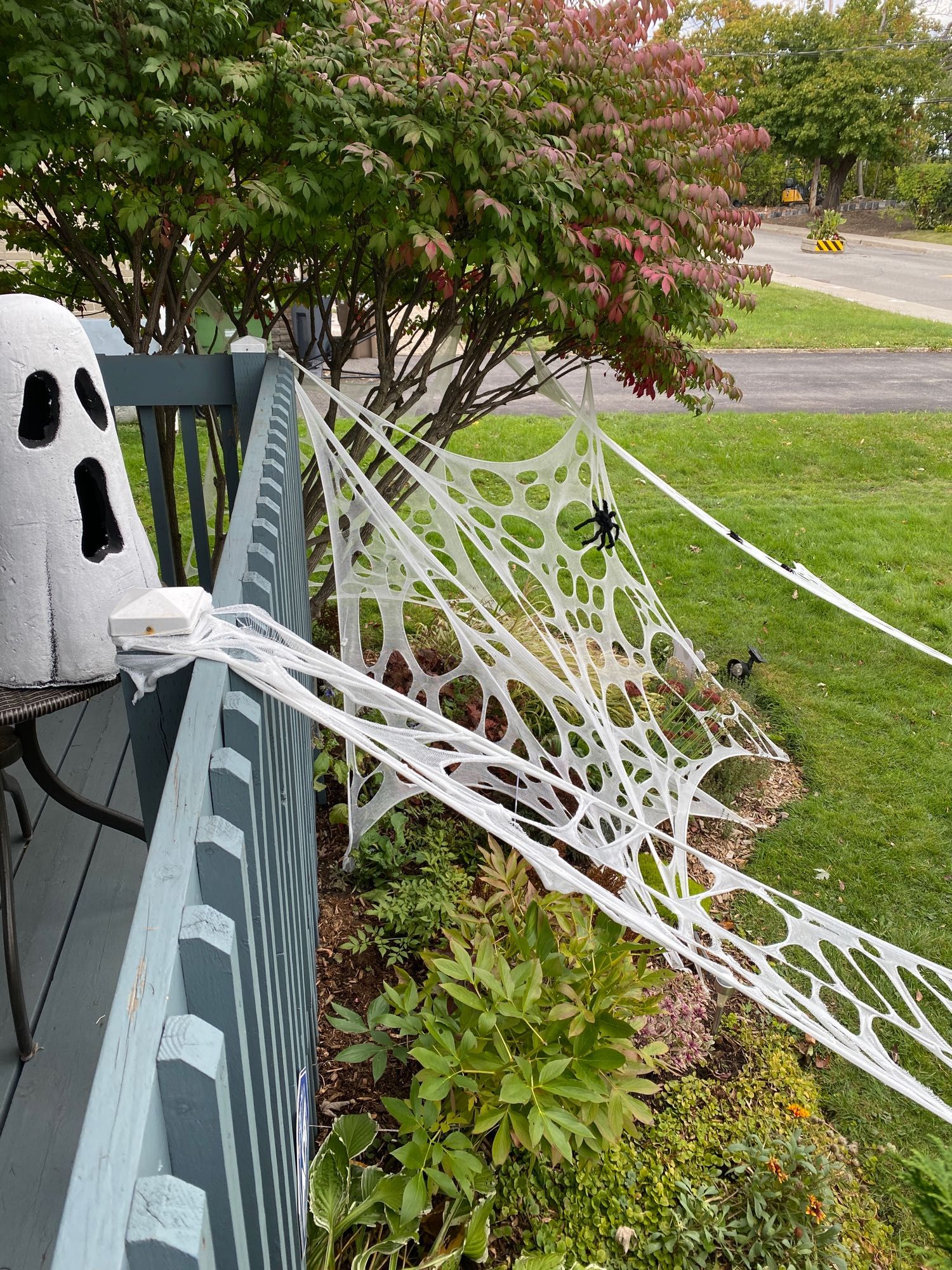 Cartoonish ghost on a balcony looks out over funny spider webs that stretch to the garden below. 